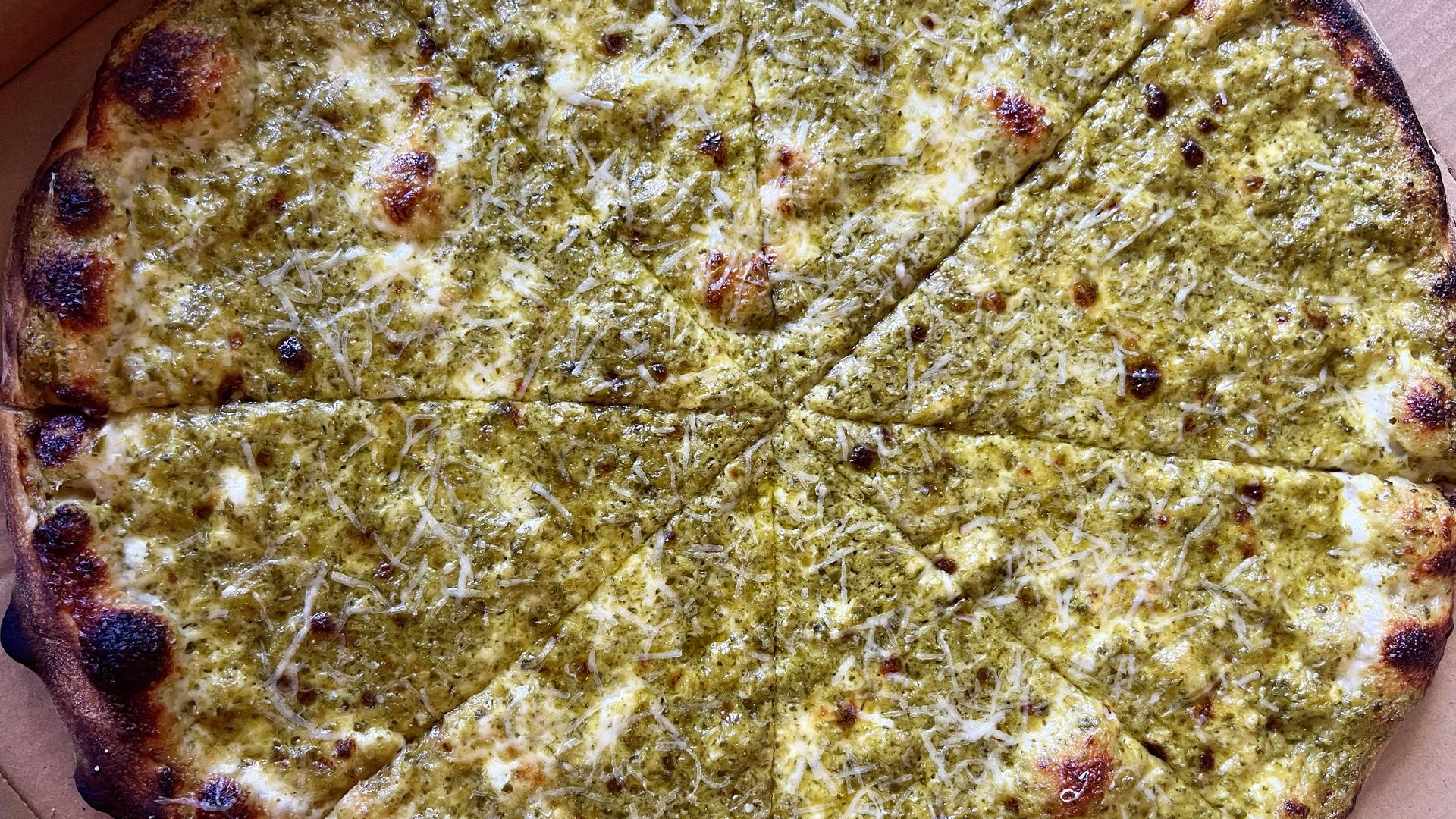 A green-colored pizza has charred crust and little cheese.