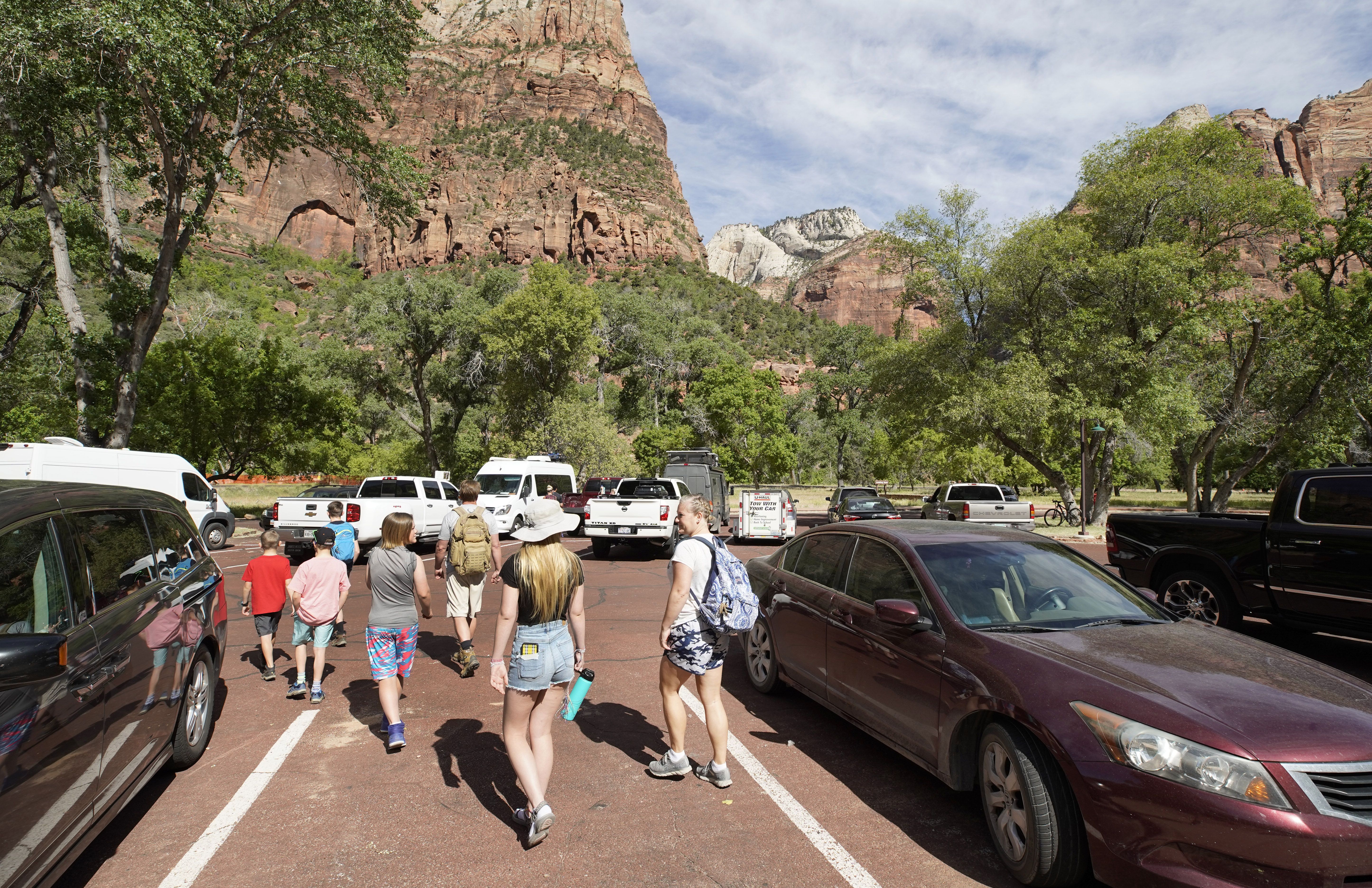 In this image, a group of people walk through a parking lot with a canyon in the background