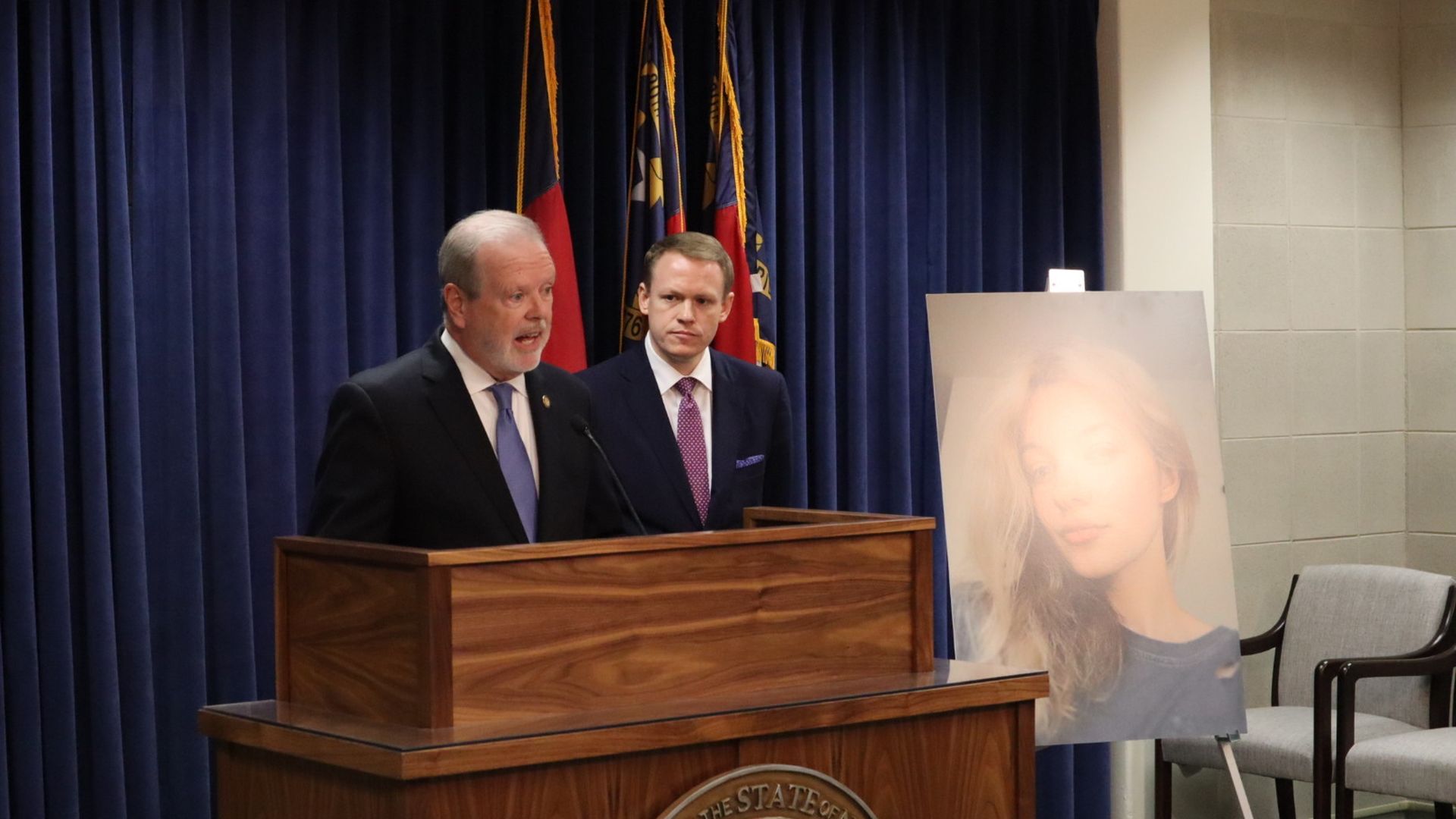 Senate leader Phil Berger, left, and House Speaker Destin Hall, right, at a wooden podium with North Carolina flags behind. A large photo of a young woman with blonde hair is displayed on an easel to the right in a conference room.