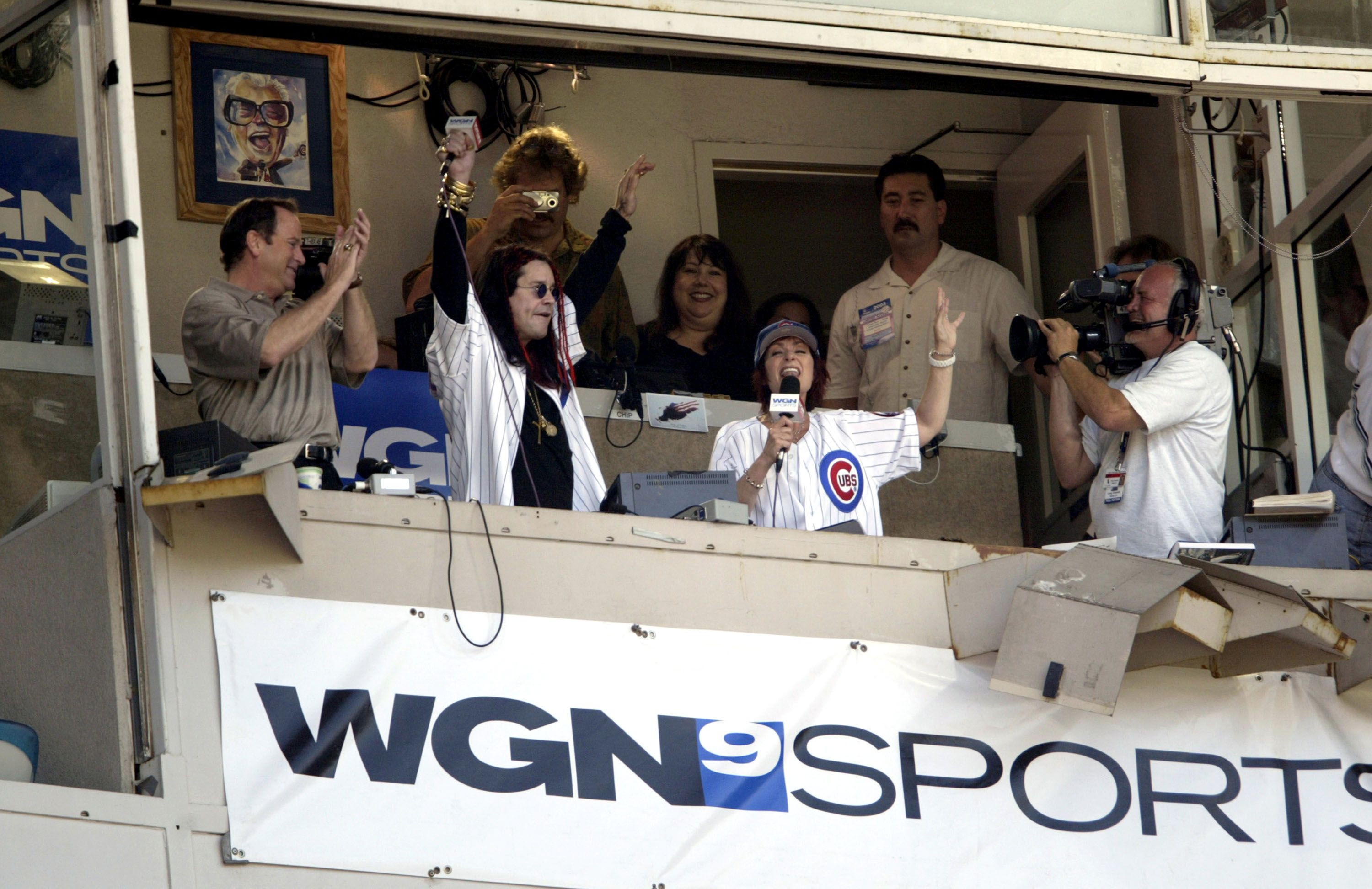 Photo of a man and woman singing in a booth at a baseball game.