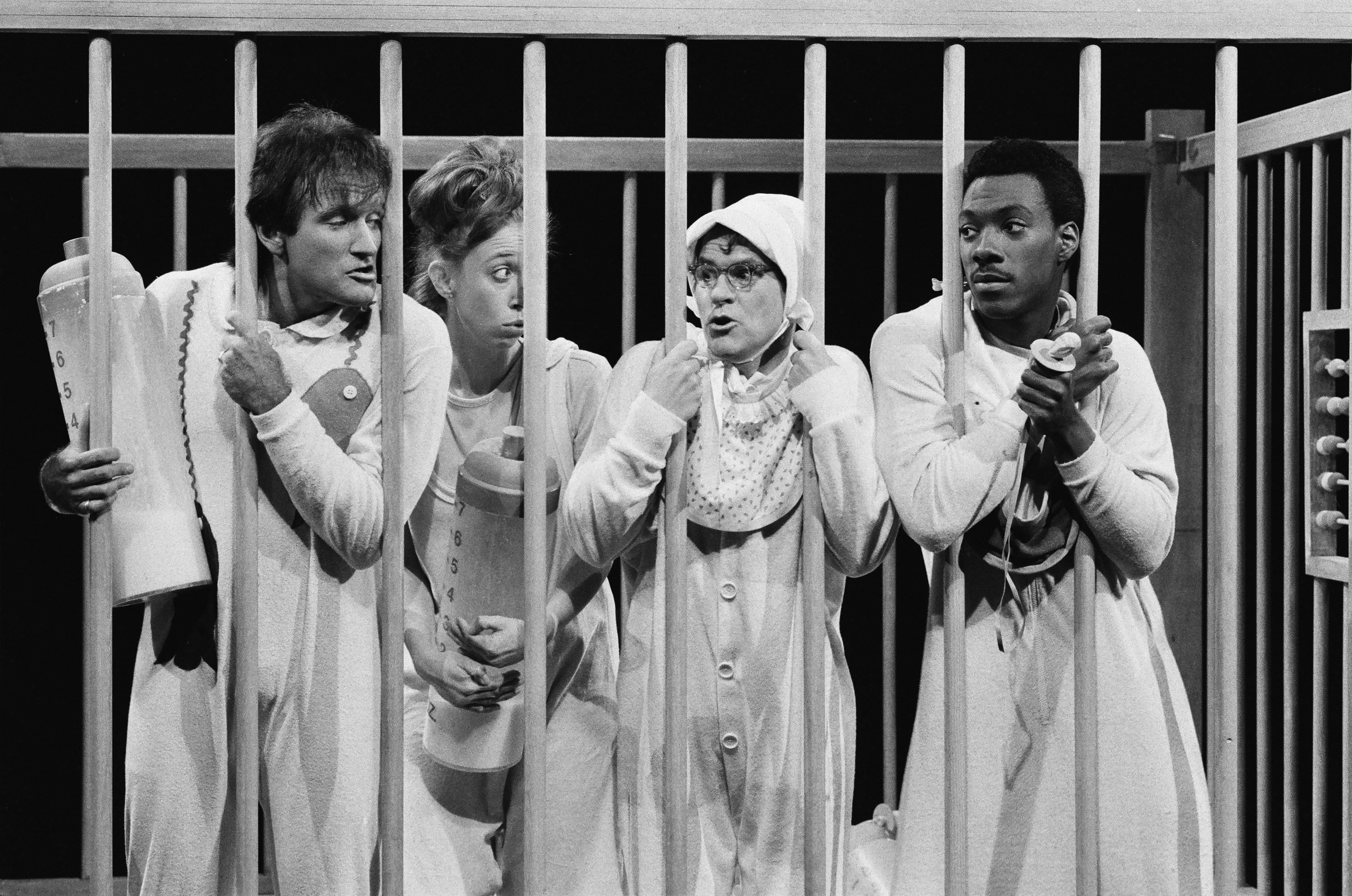 Photo of actors dressed up like babies in a crib for a comedy sketch on television. 