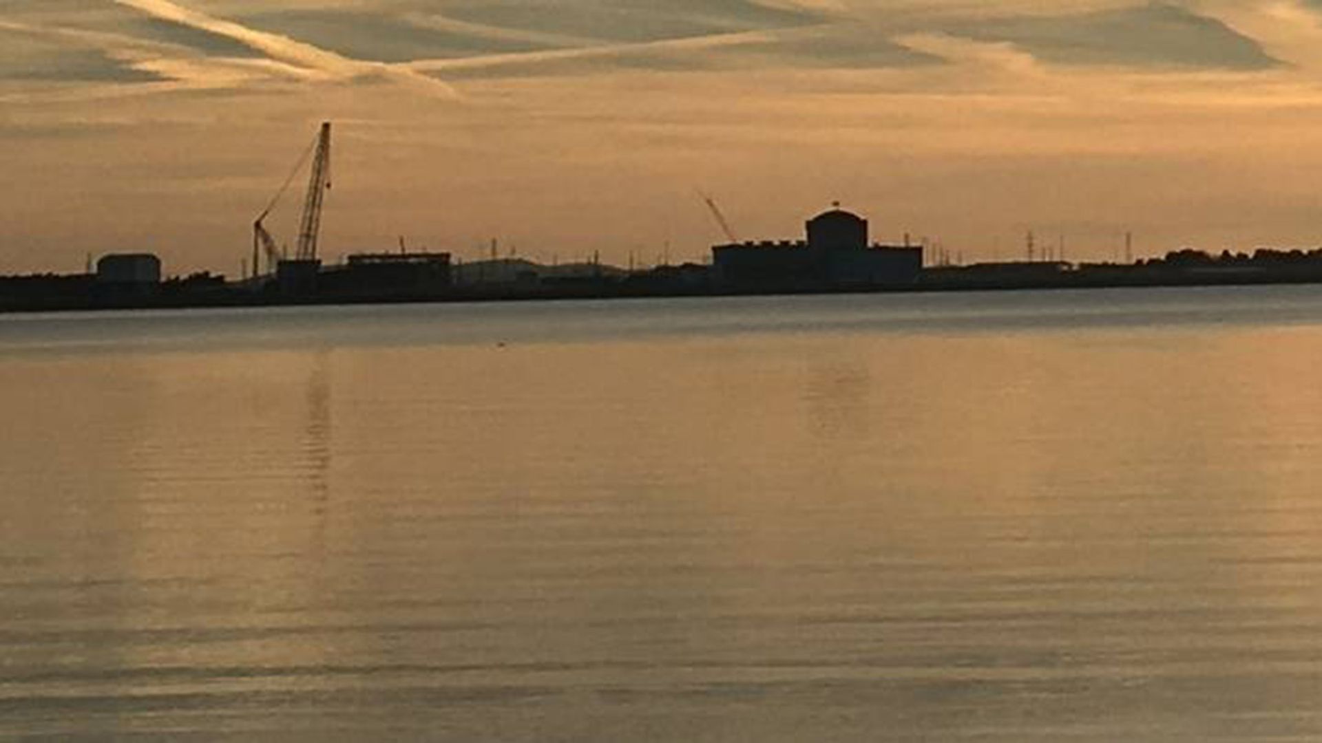A photo of V.C. Summer Nuclear Plant, on the shore of Lake Monticello, with an orange sky at dusk or at dawn in the background.
