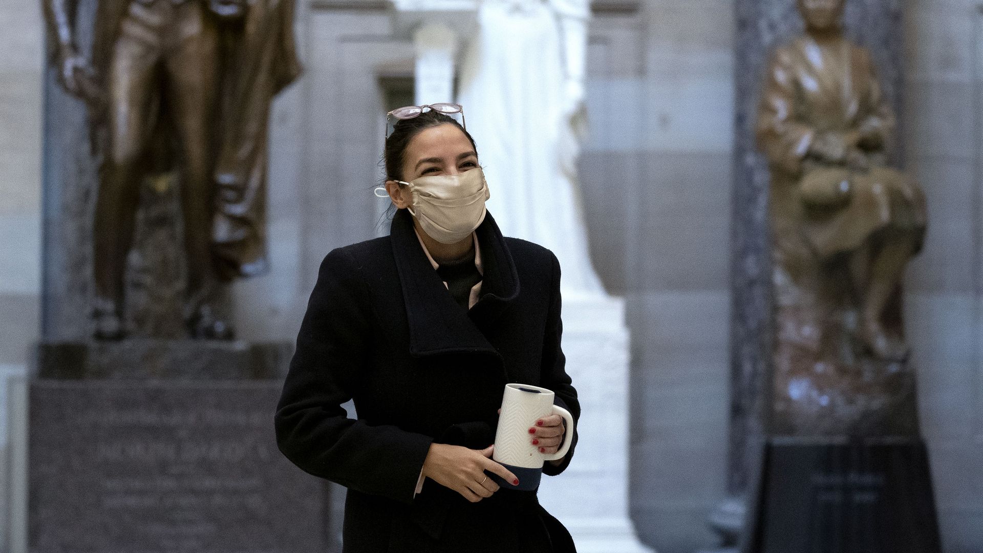 Picture of Rep. Alexandria Ocasio-Cortez wearing a brown mask and holding a mug
