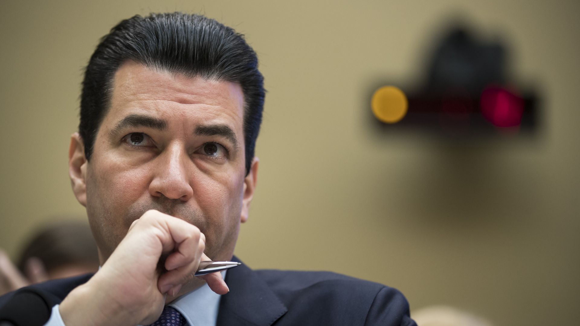 In this image, FDA commissioner Scott Gottlieb sits with a hand covering his mouth as he frowns into the distance beyond the camera. 