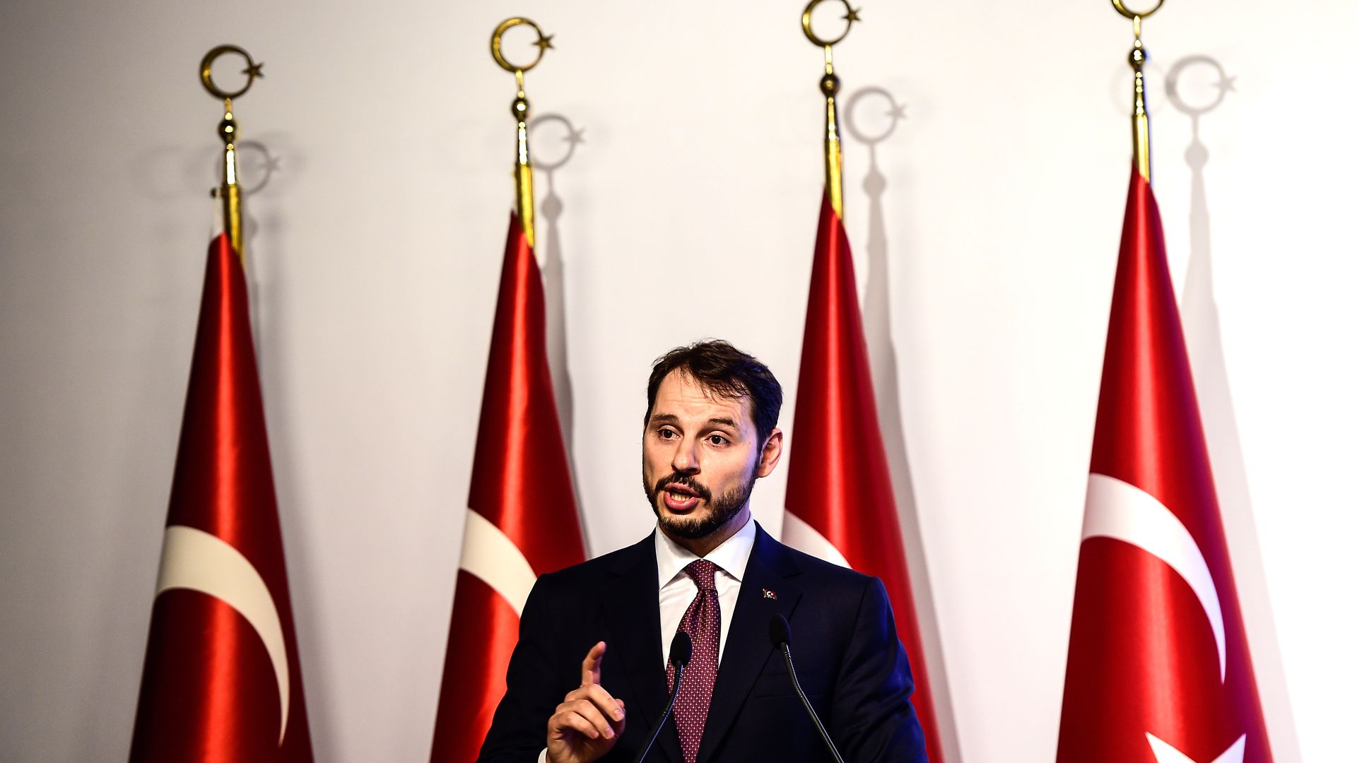 Turkish finance minister giving a speech in front of four red flags