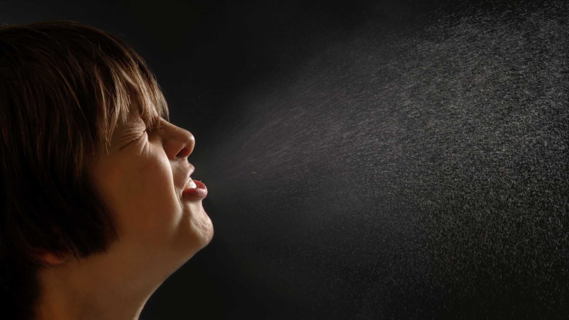 Boy sneezing with droplets highlighted in the air