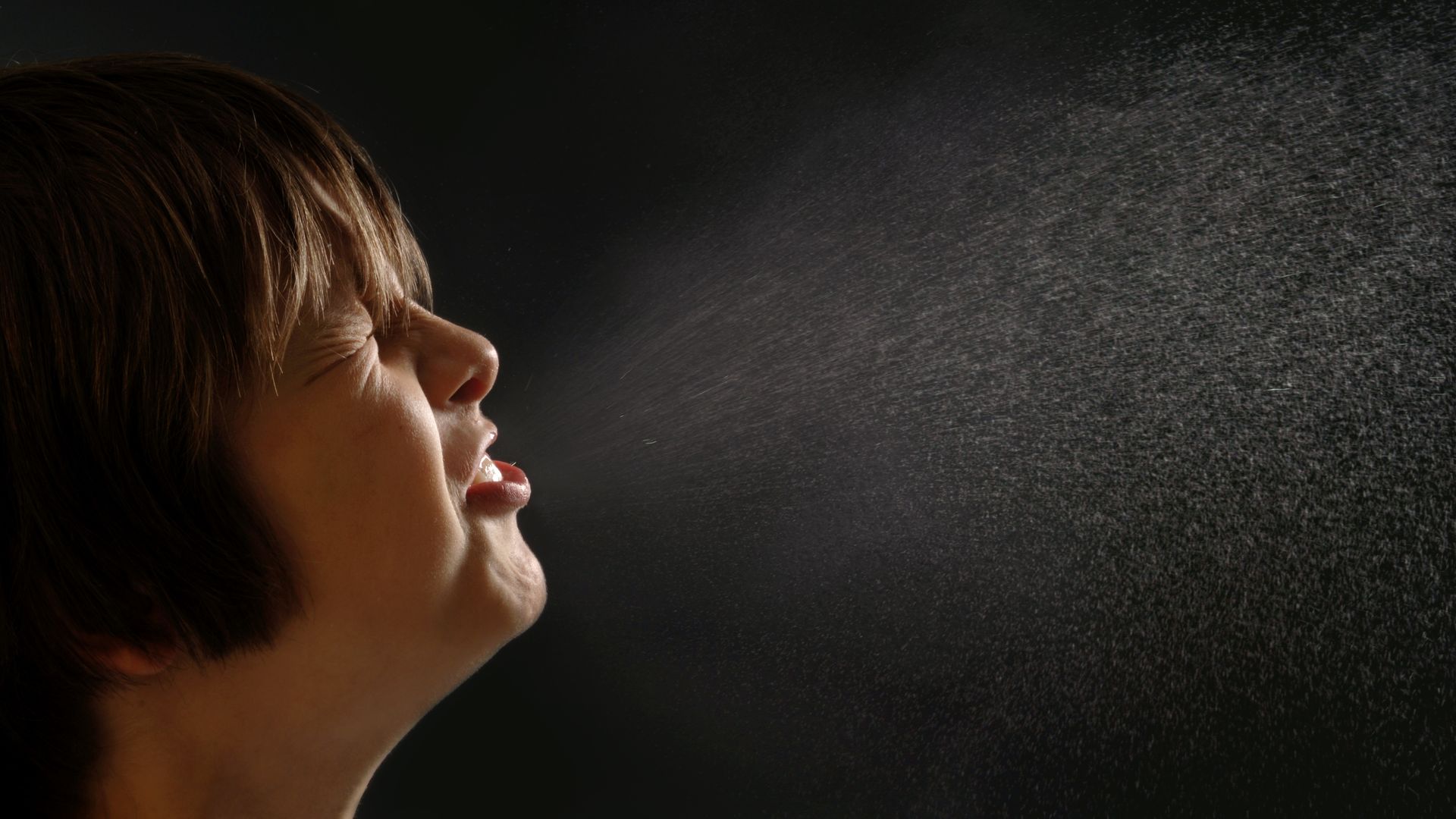 Boy sneezing with droplets highlighted in the air