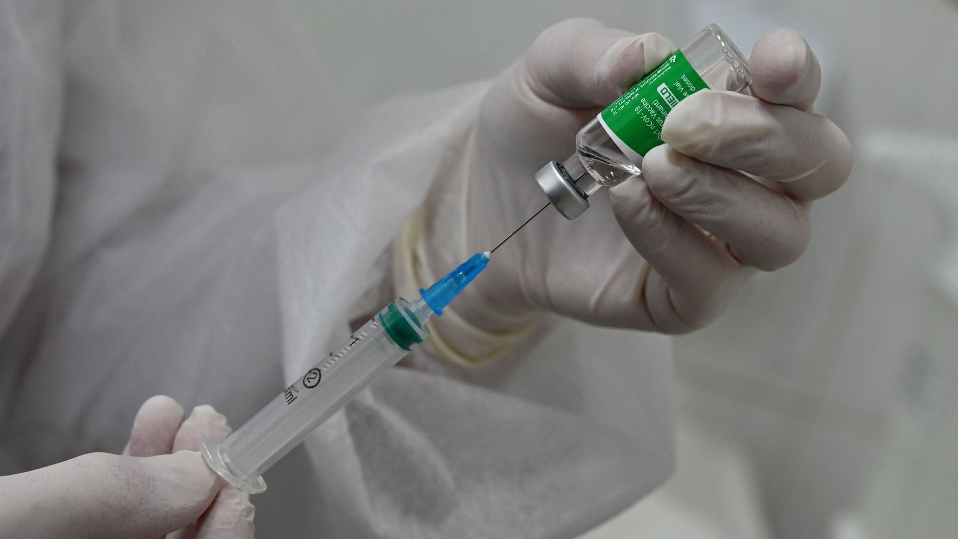 Photo of two hands holding up a shot of the AstraZeneca COVID-19 vaccine