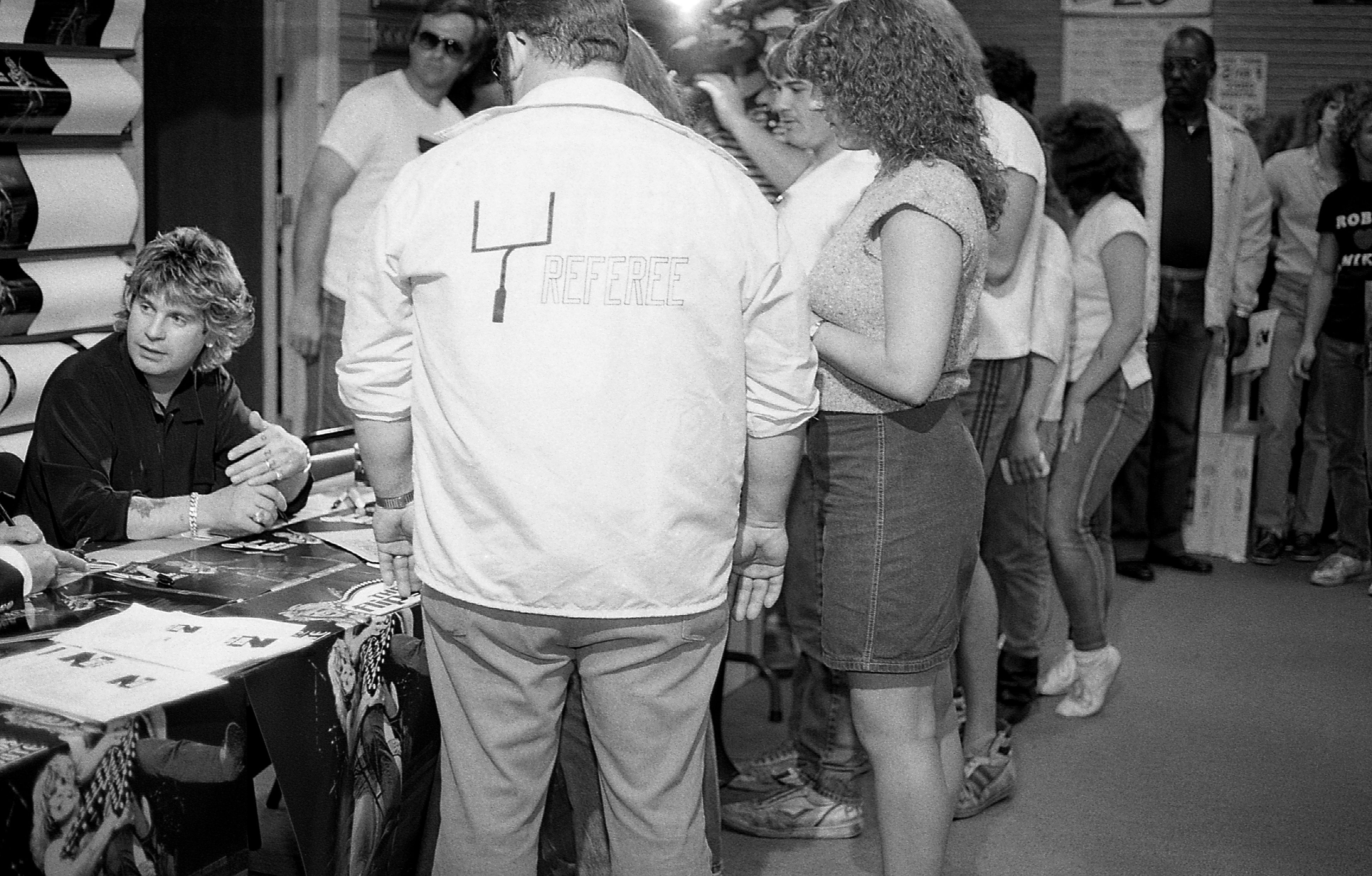 Photo of a man signing autographs in front of a table of people.