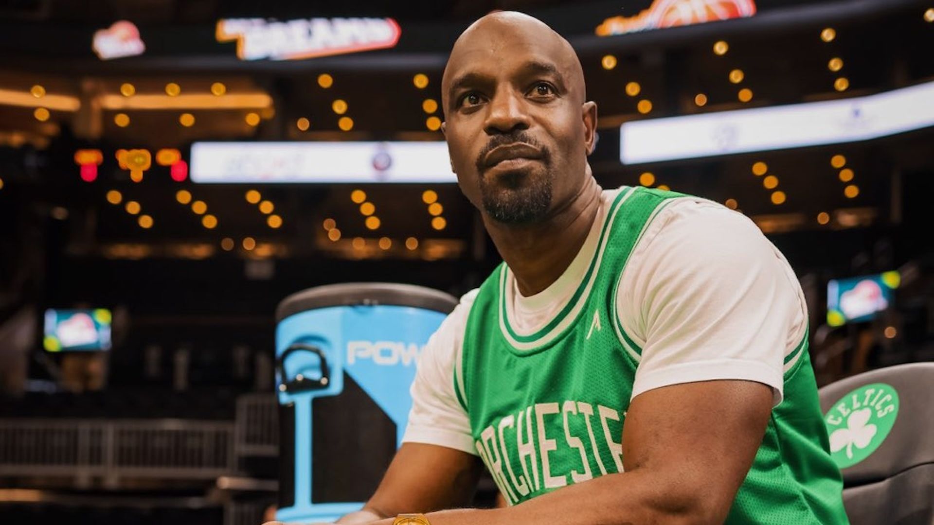 Peda Edouard, founder of Mathmatik Athletics, wears a Dorchester jersey while sitting in TD Garden.