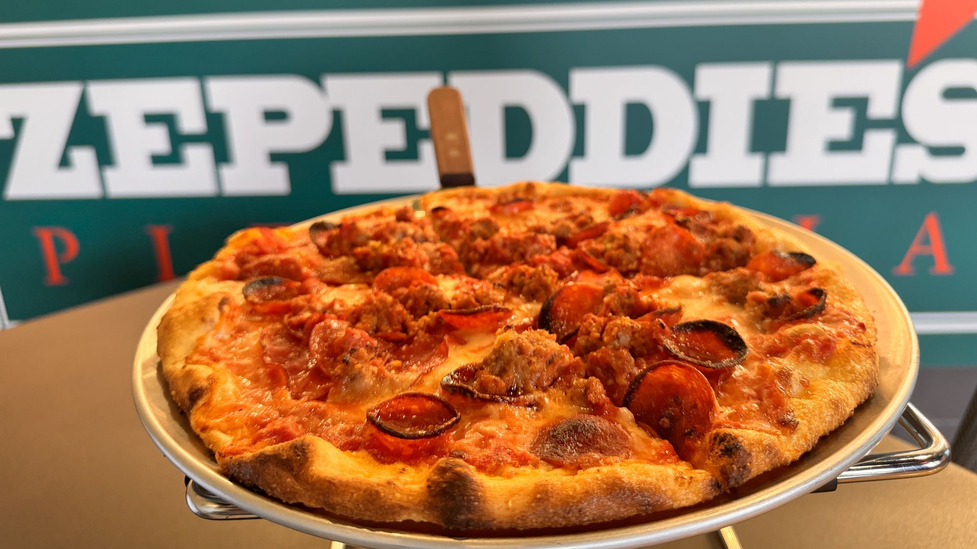 pizza pie with sign that reads "zepeddie's" behind it
