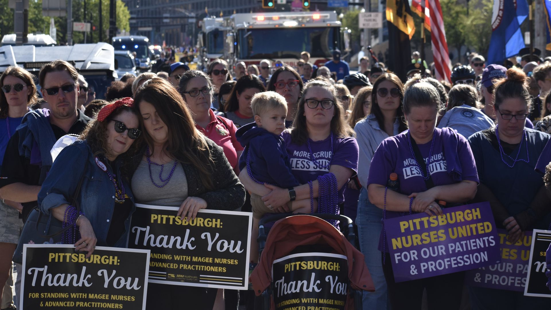 A crowd of people, including nurses wearing purple shirts and beads, hold signs thanking Pittsburgh for supporting Magee nurses and advanced practitioners during a street gathering.