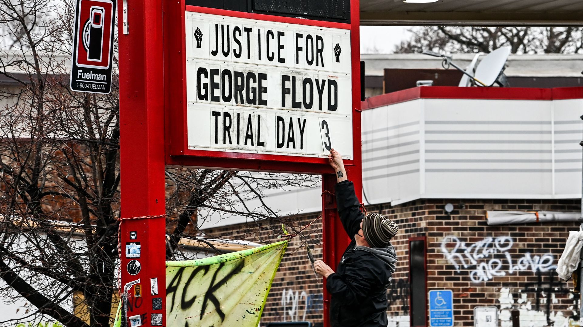 A person puts up a sign saying Justice for George Floyd Trial Day 3