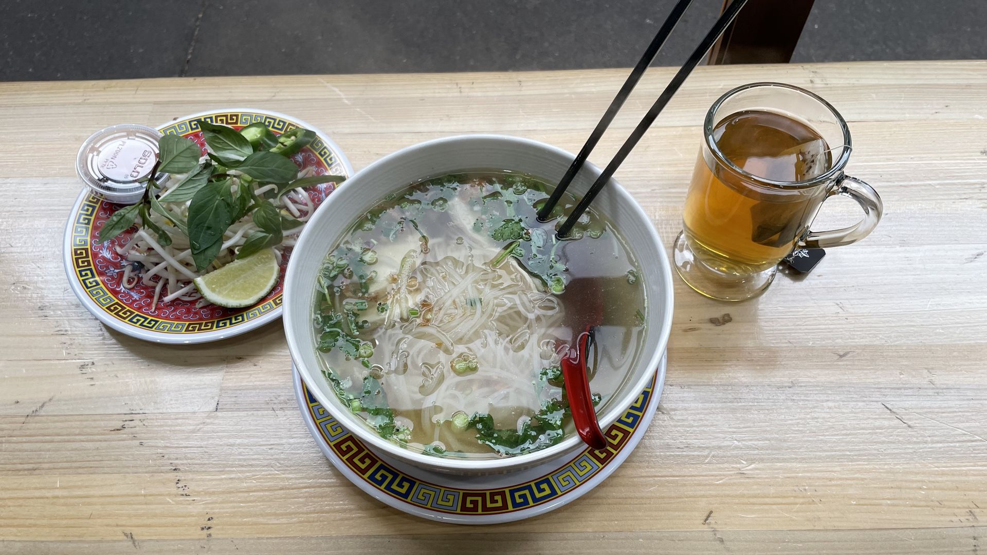 A photo of a bowl of noodle soup next to a cup of tea.