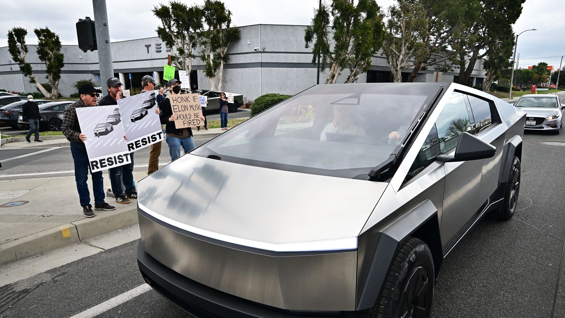 A Cybertruck passes by Tesla protesters 