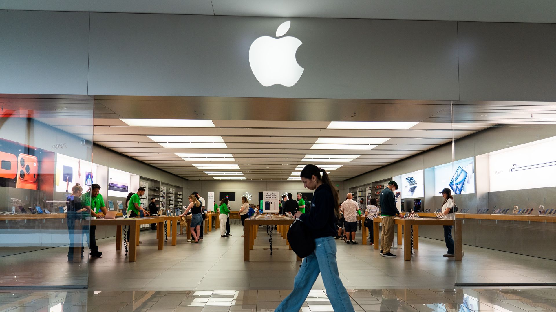 A woman walking past an Apple store in a mall.