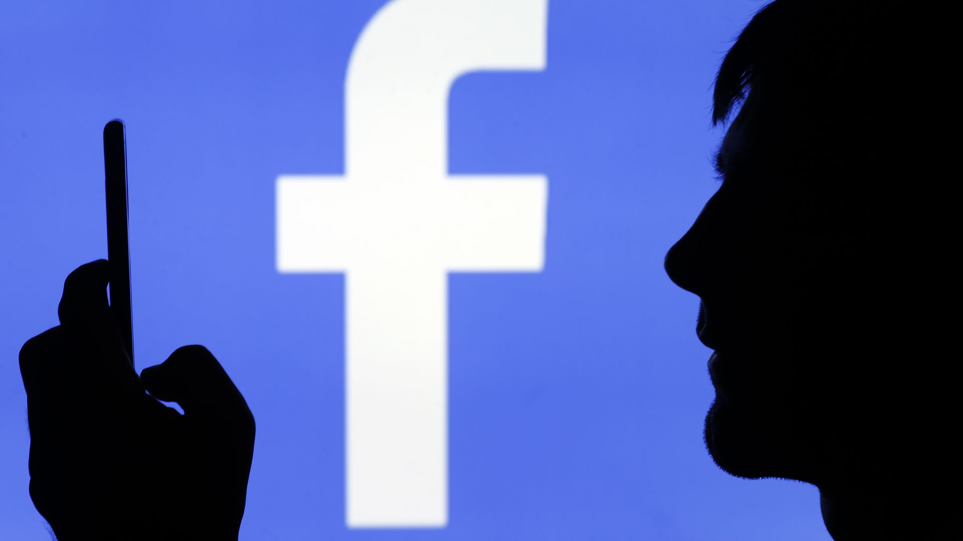 Someone holds a cell phone with the Facebook logo in the background.