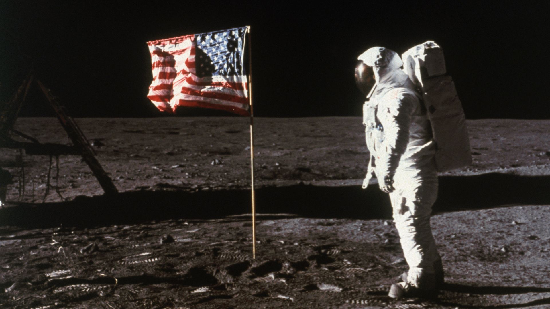 Buzz Aldrin stands beside an American flag on the Moon.