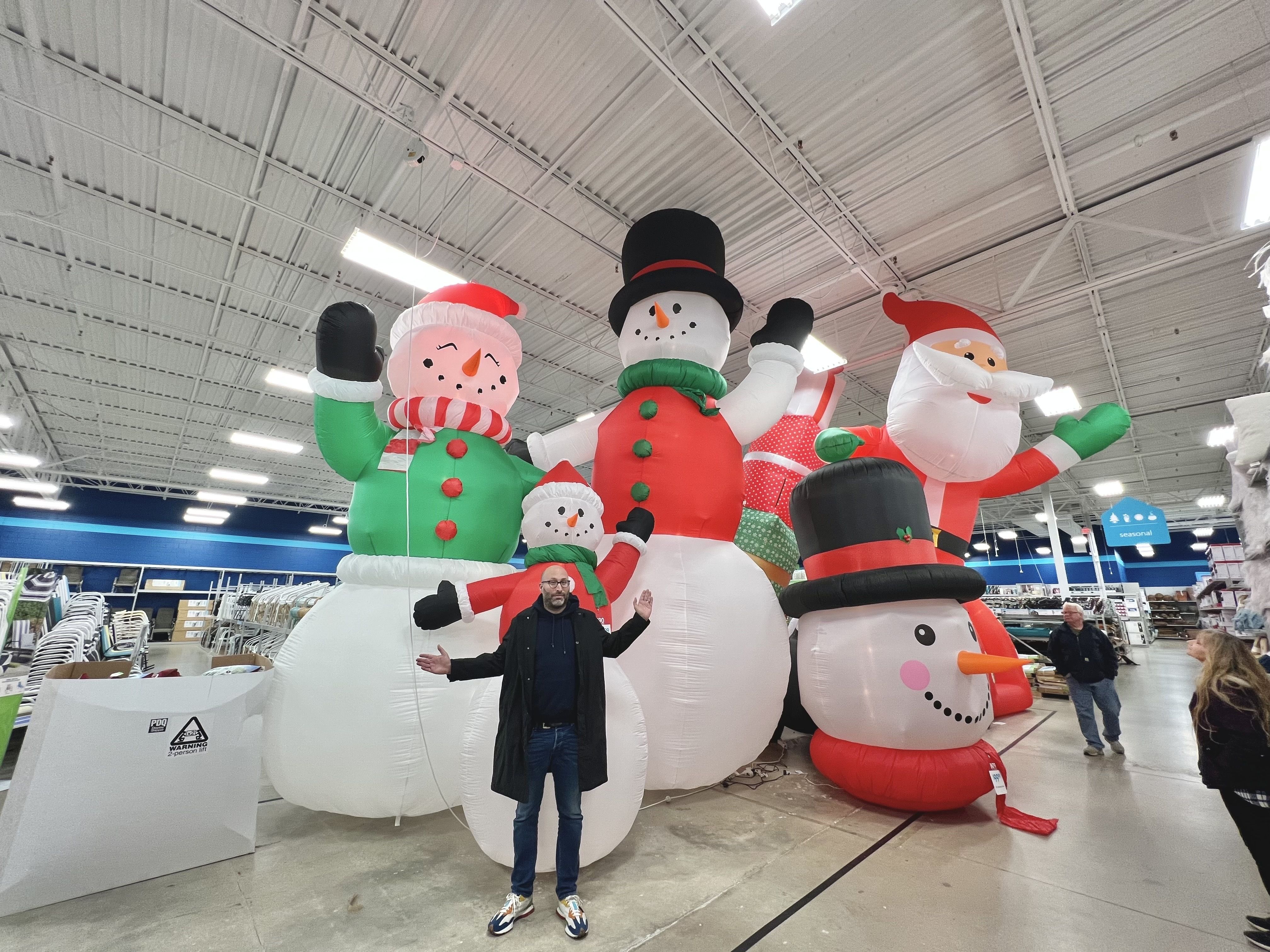 Photo of a man standing in front of inflatable snowmen in store.