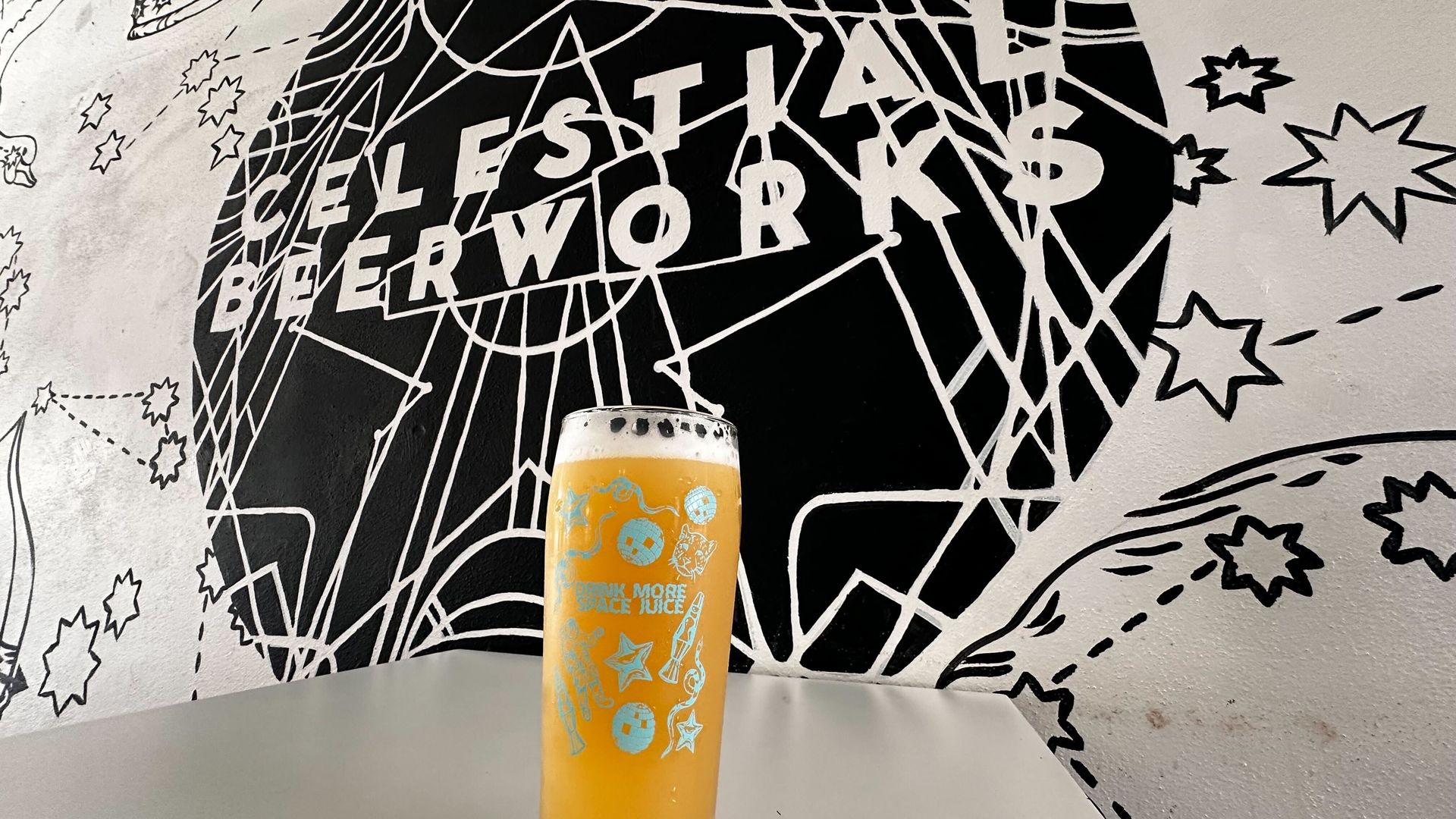 A photo of a beer in a pint glass in front of a mural