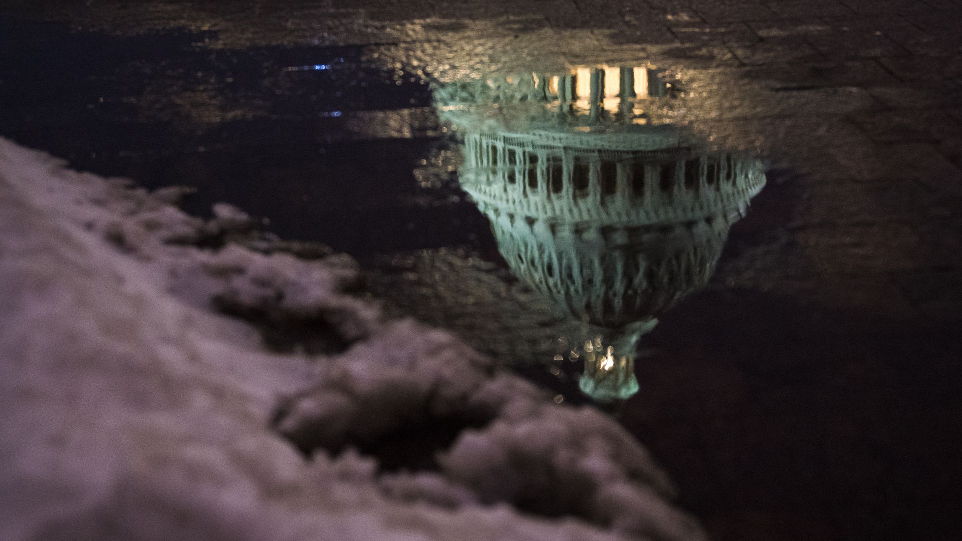 The Capitol dome is reflected in a puddle at dusk.