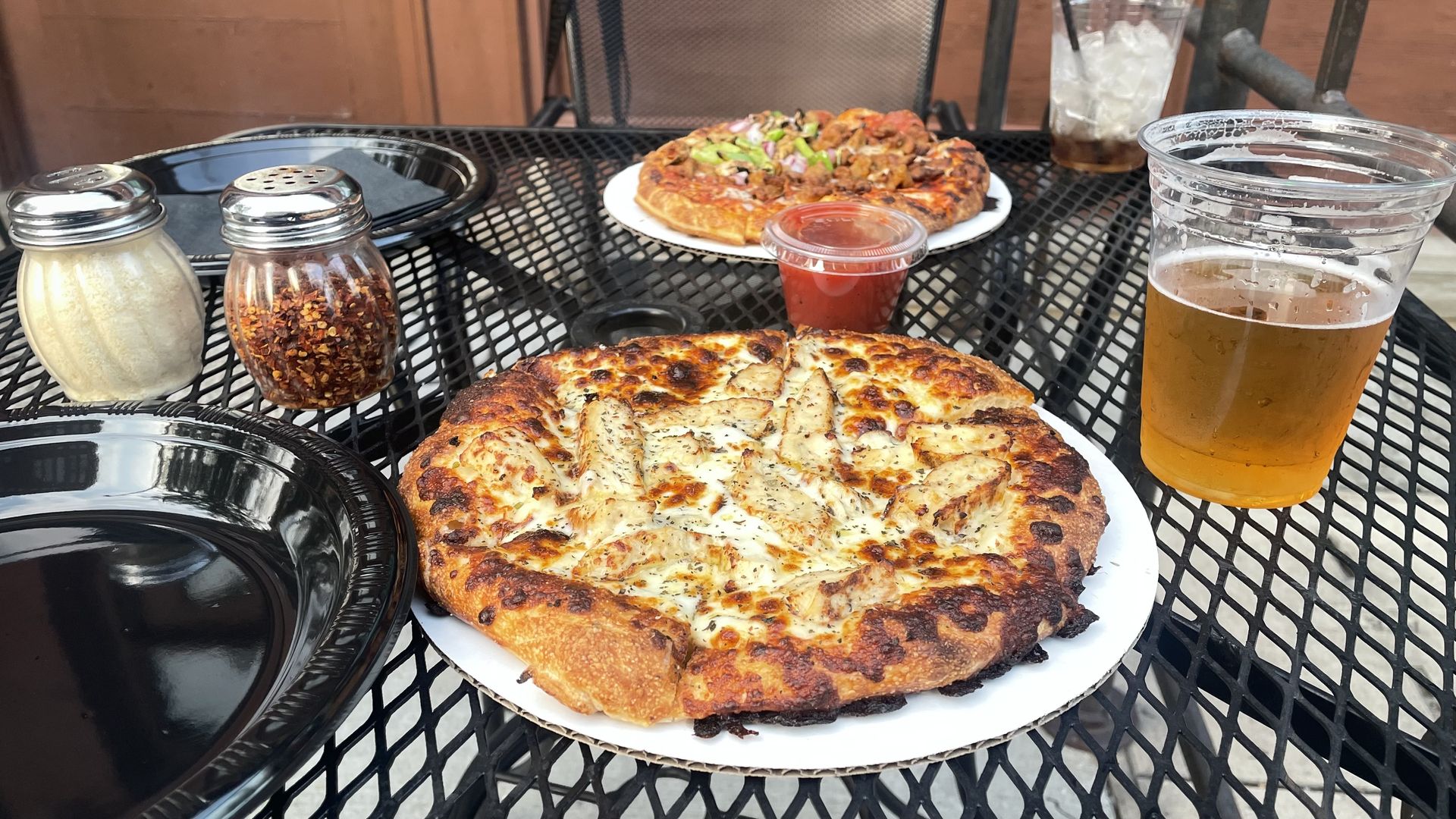 A white pizza on an outdoor metal mesh table with a beer next to it