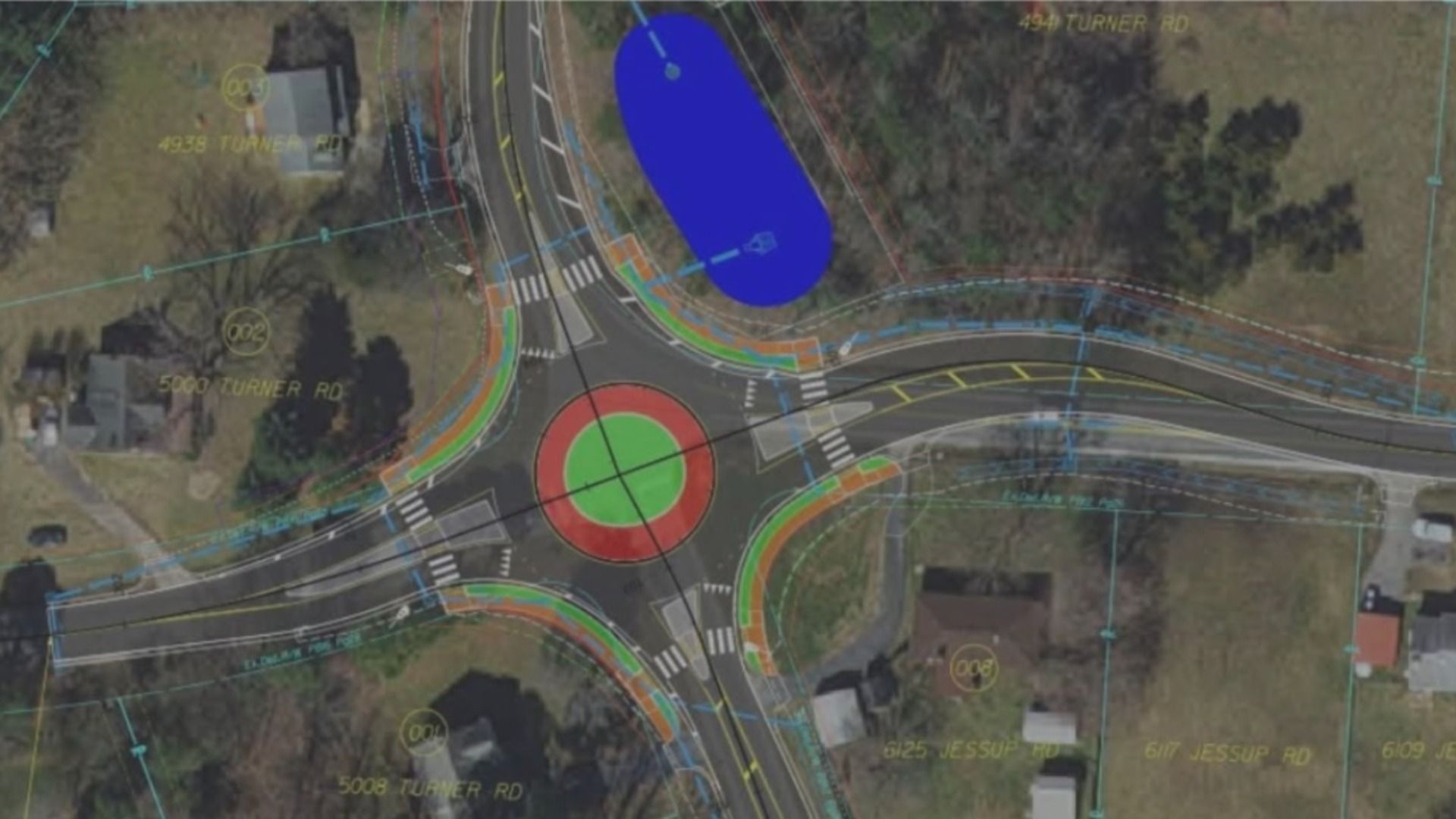 An aerial view of a road roundabout with colored lane markings and architectural overlays; a large blue oval area and a red-green circular central island are visible among curved roads and trees.