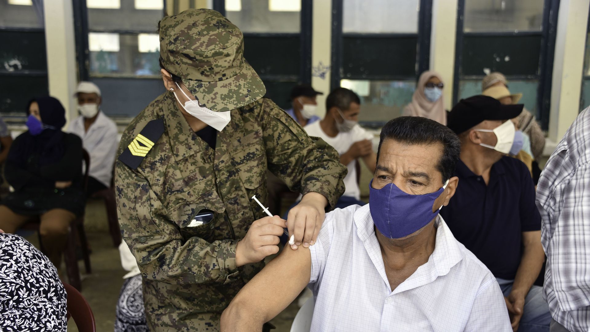 An army officer administers a vaccine to a man with face mask 