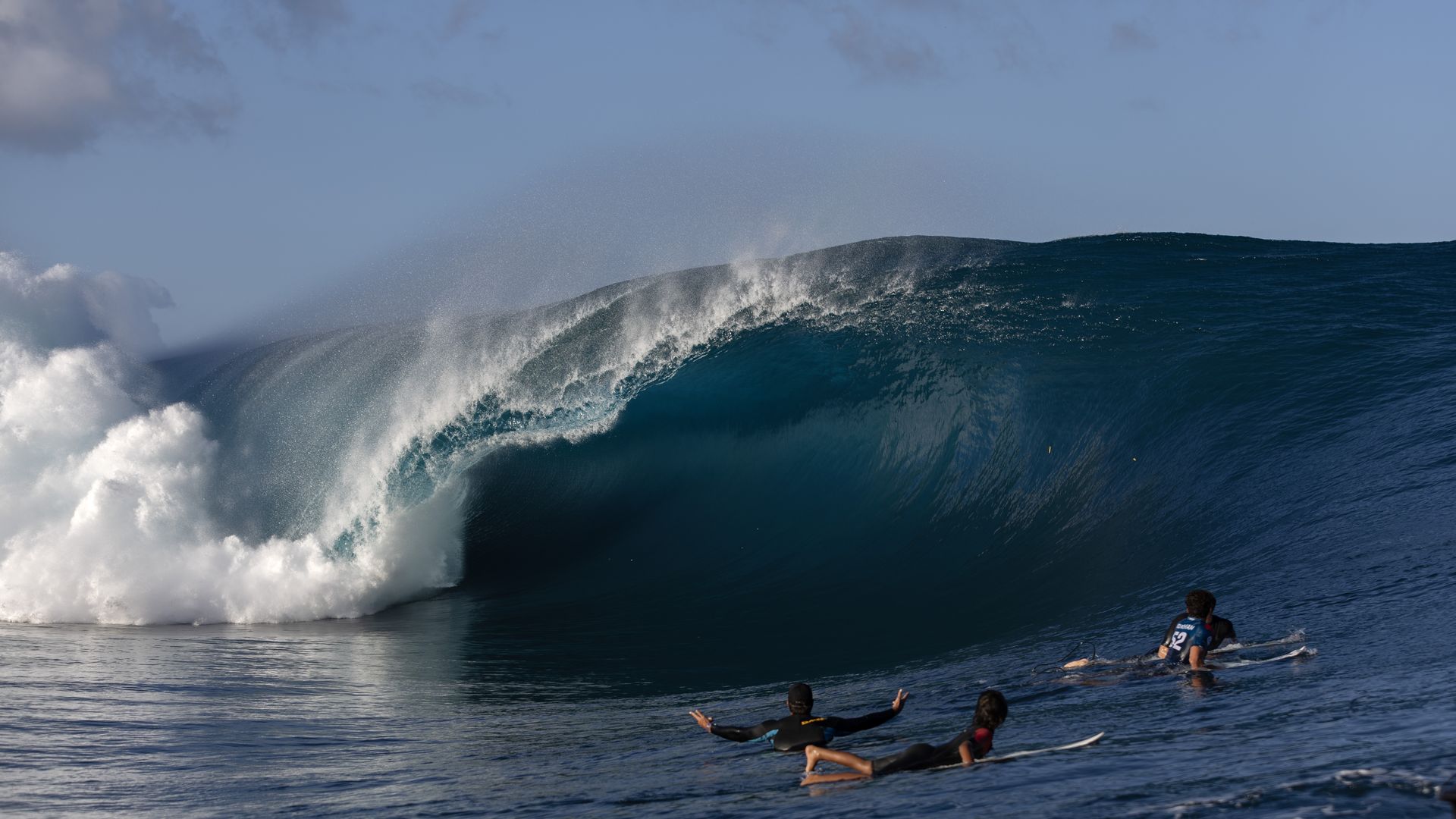 Surfers watch a wave crash in Teahupo'o.