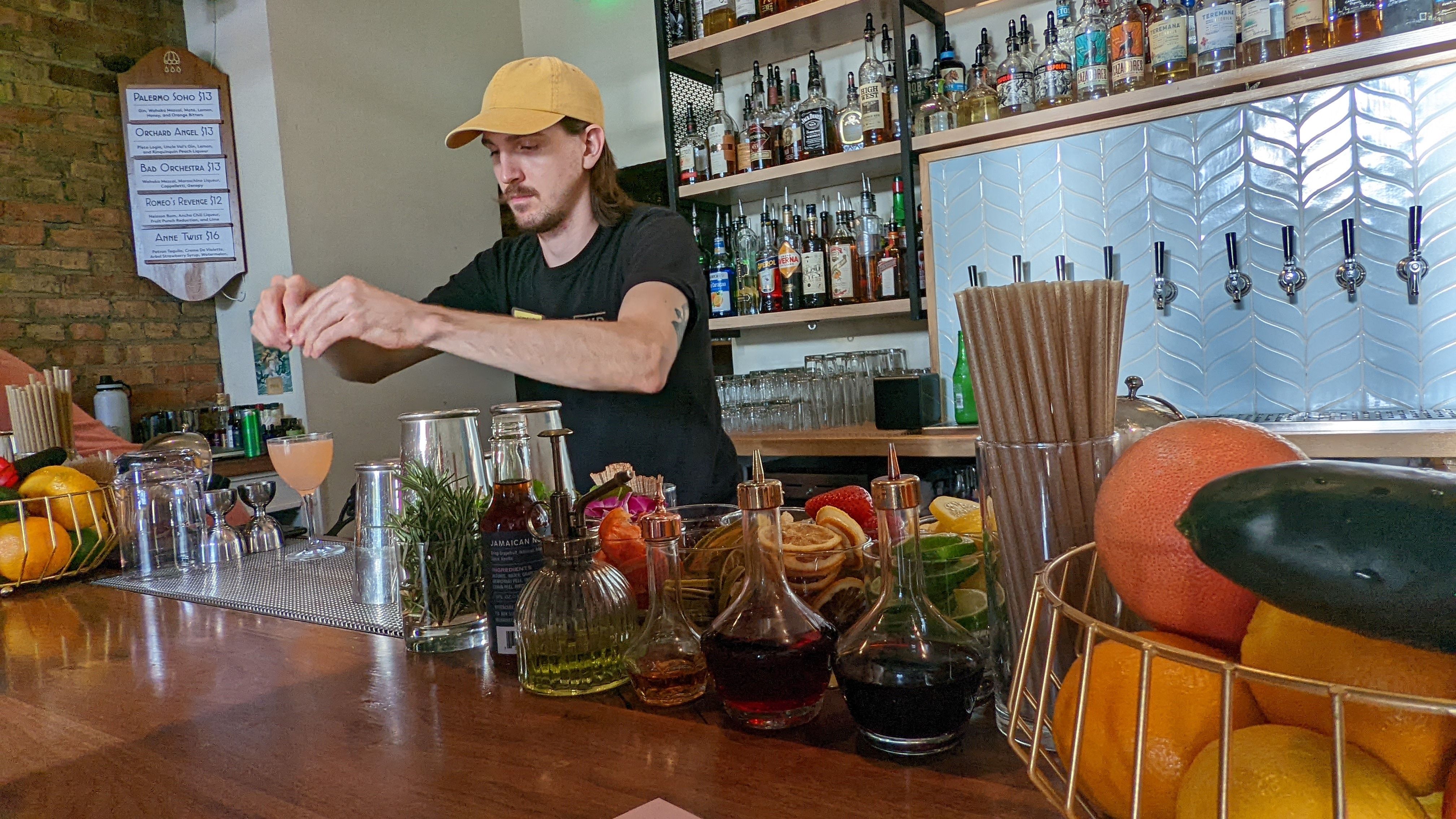 A bartender prepares a cocktail behind a bar full of fresh fruits and herbs.