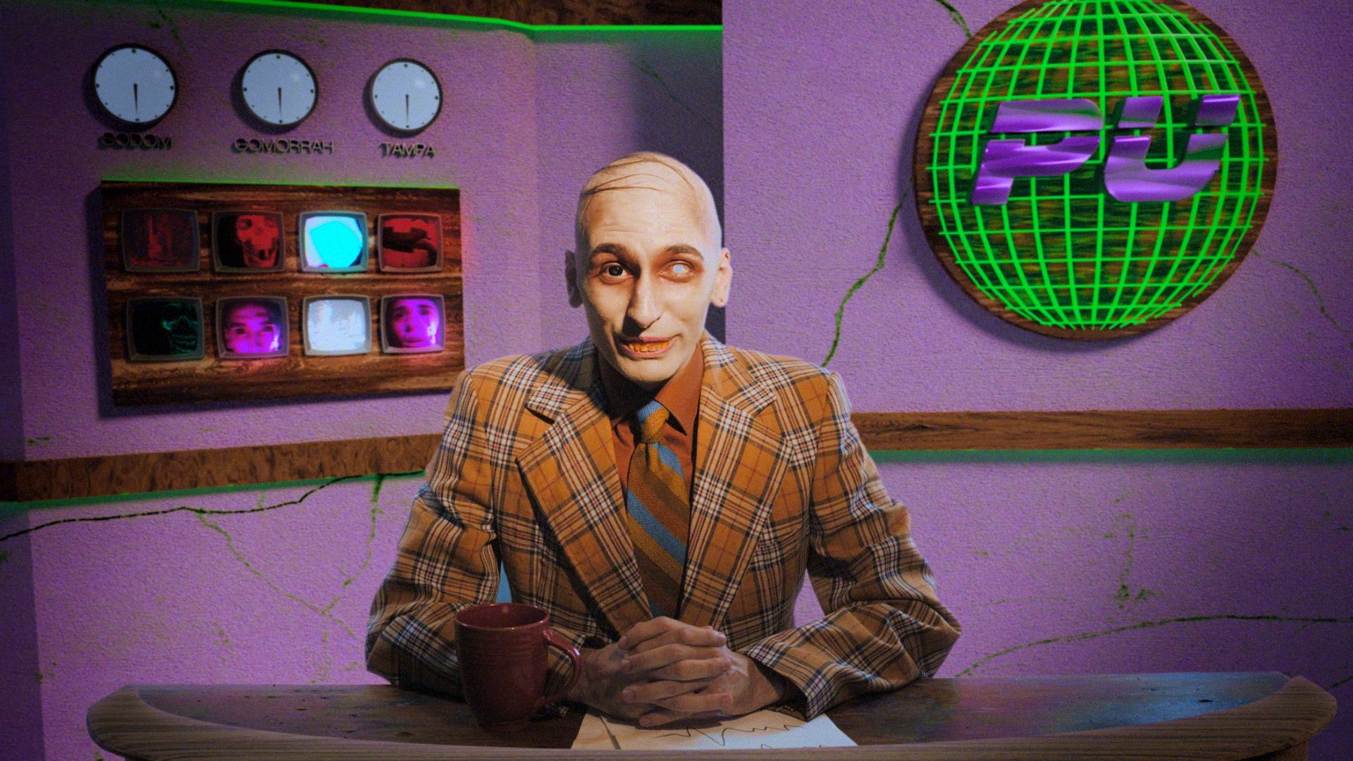 A TV news anchor in an orange plaid suit with one eye sits at a desk with his hands folded