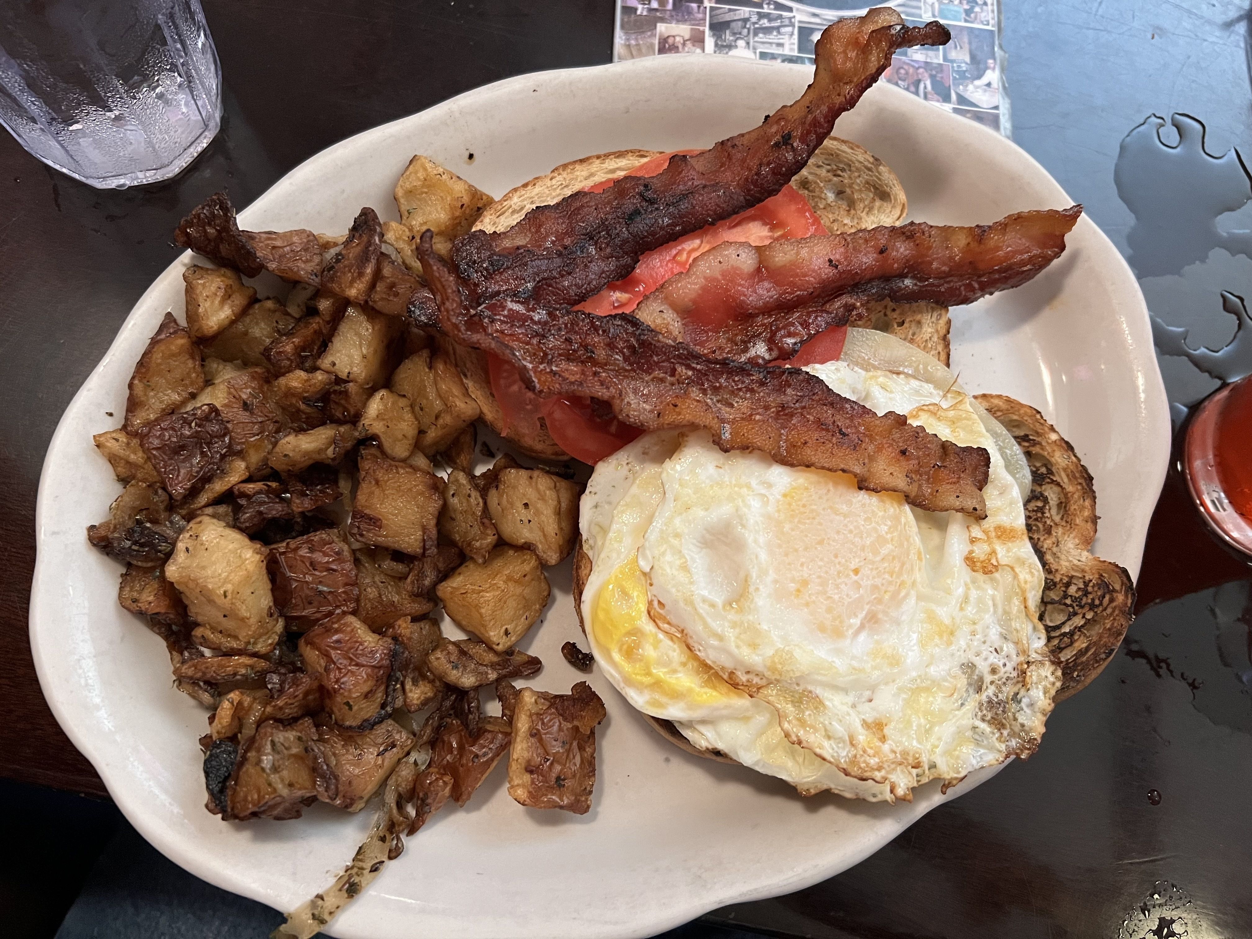 A plate of homefries with bacon, egg, tomato and bread