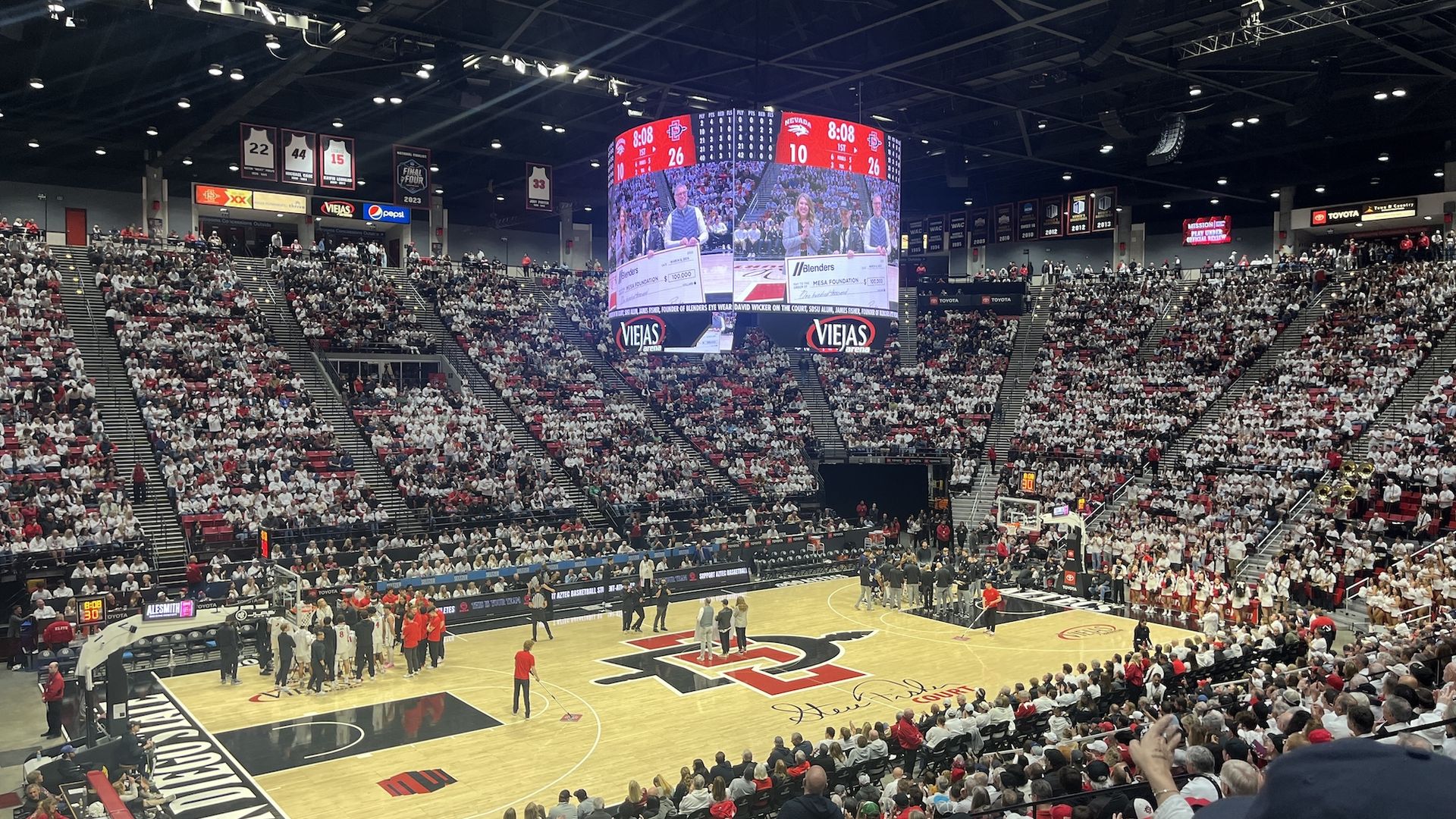 A view inside the SDSU basketball arena with teams huddled at halftime. 
