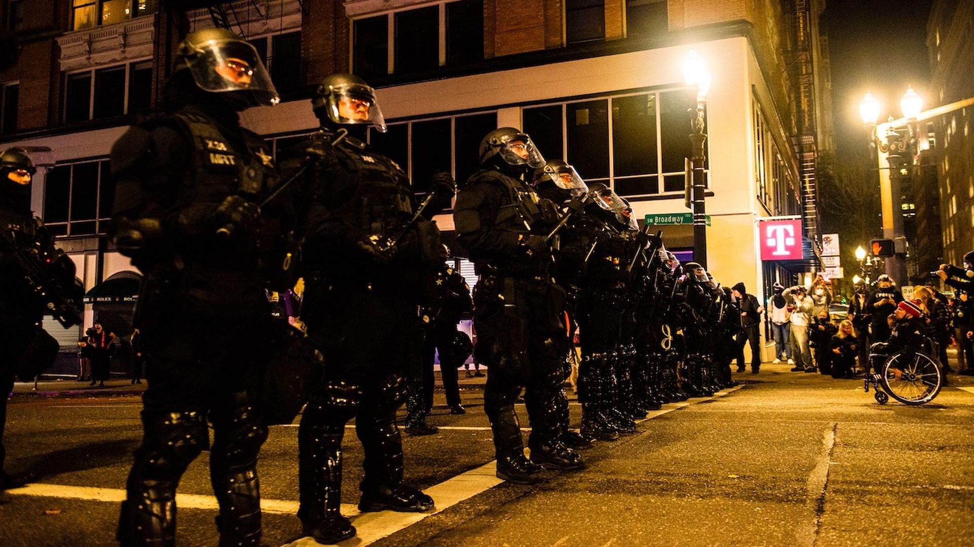A photo showing a row of police officers wearing black riot gear facing a group of protestors.