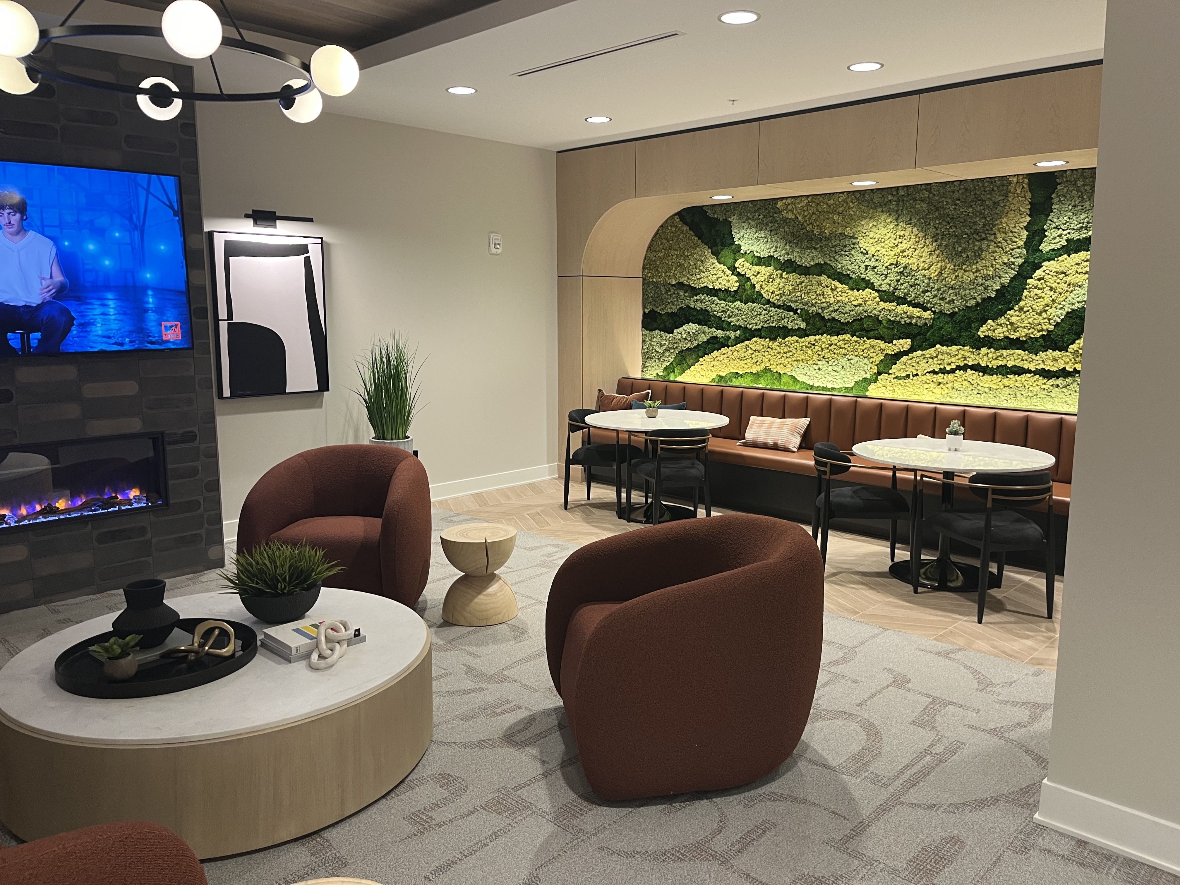 A lounge area with a TV, chairs, tables and a green wall 