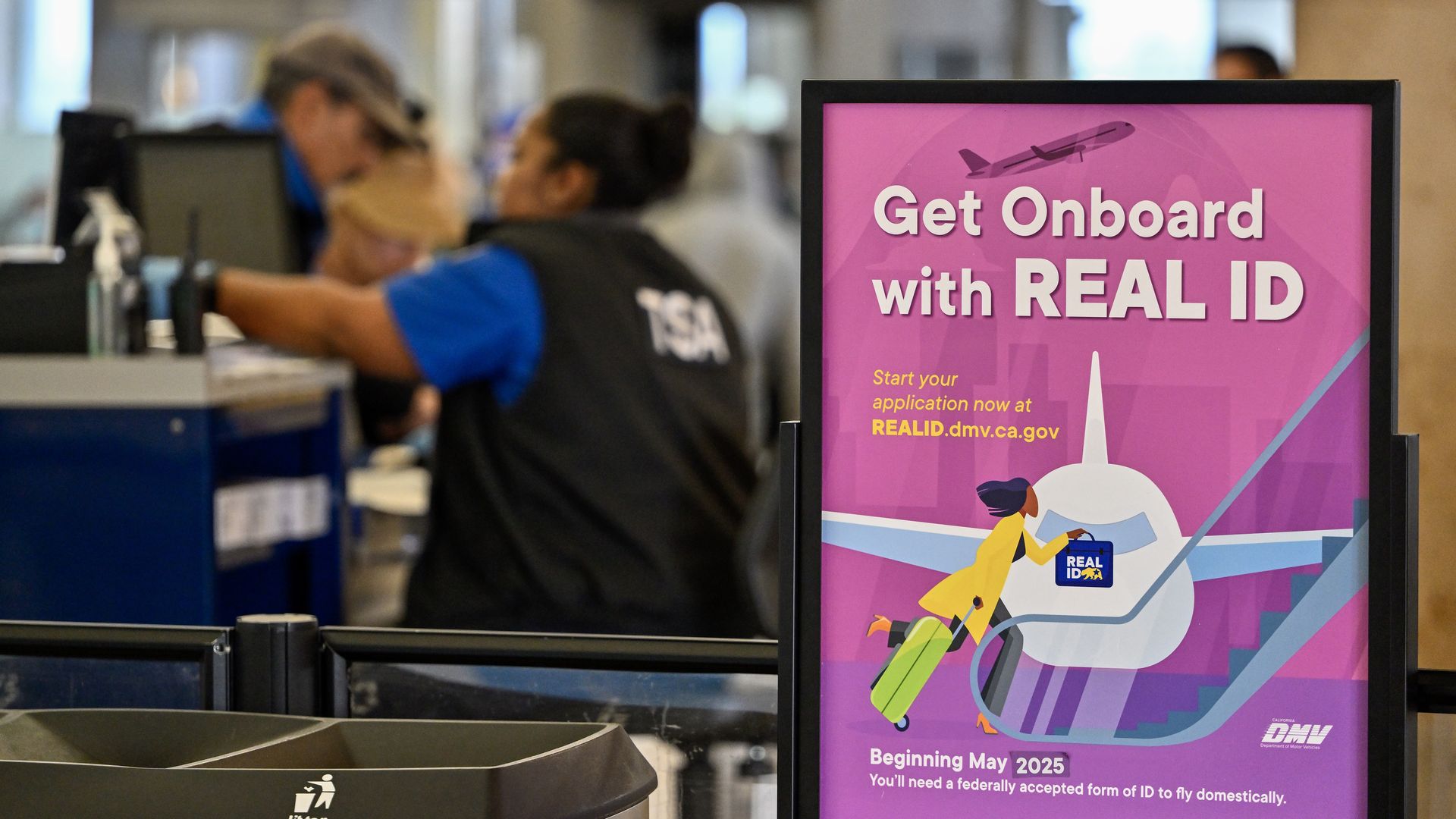 A pink sign saying "Get Onboard with REAL ID" is displayed at a TSA security checkpoint at a California airport.
