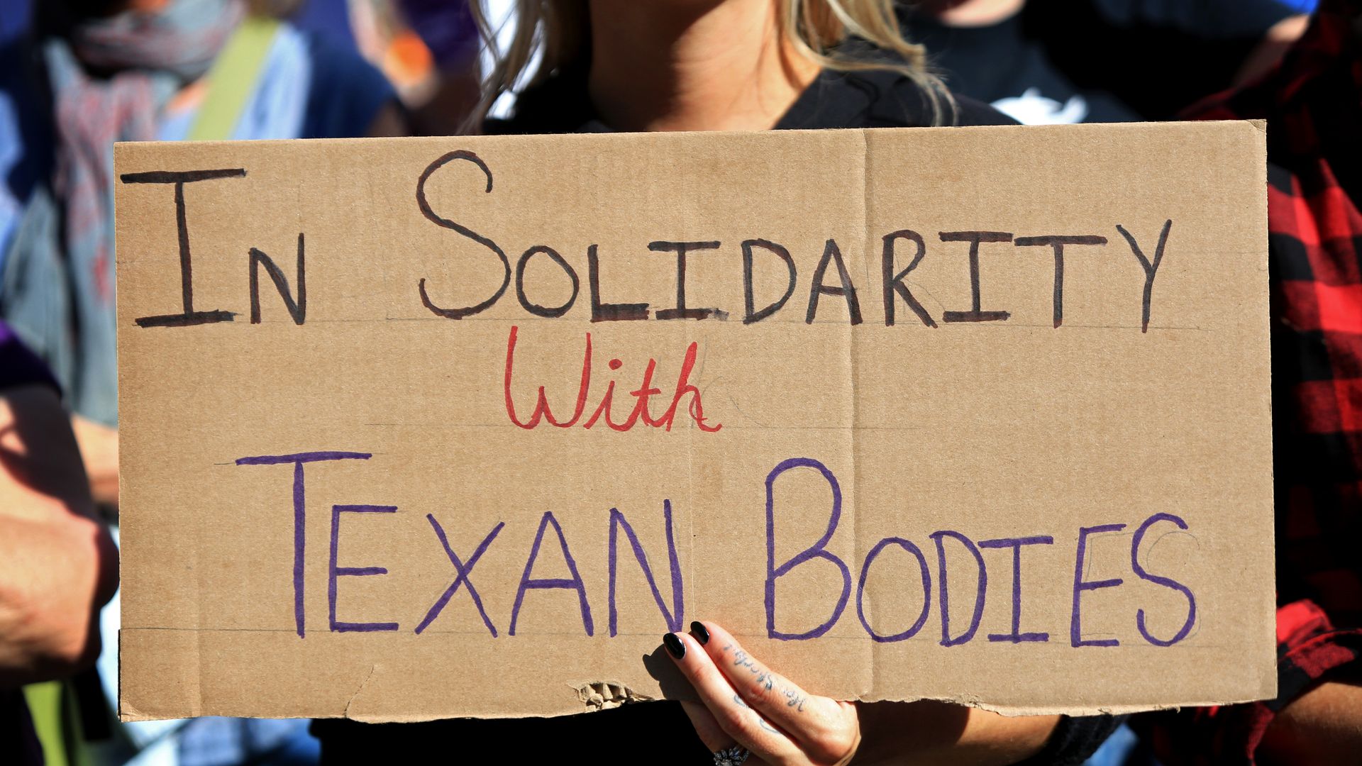 Photo of a person holding a sign that says "in solidarity with Texan bodies"