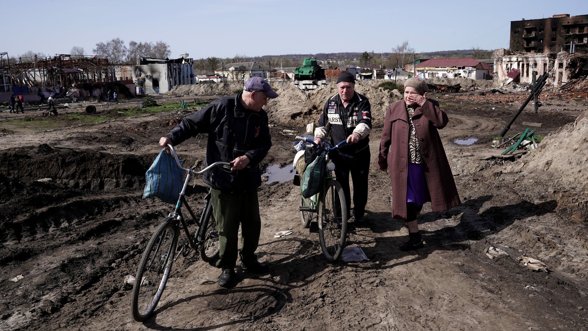 Two men pushing bicycles and a woman walk past the buildings destroyed as a result of Russian shelling 