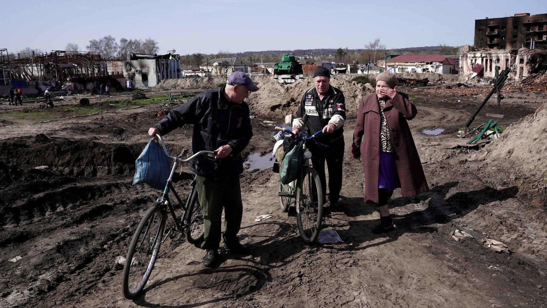 Two men pushing bicycles and a woman walk past the buildings destroyed as a result of Russian shelling
