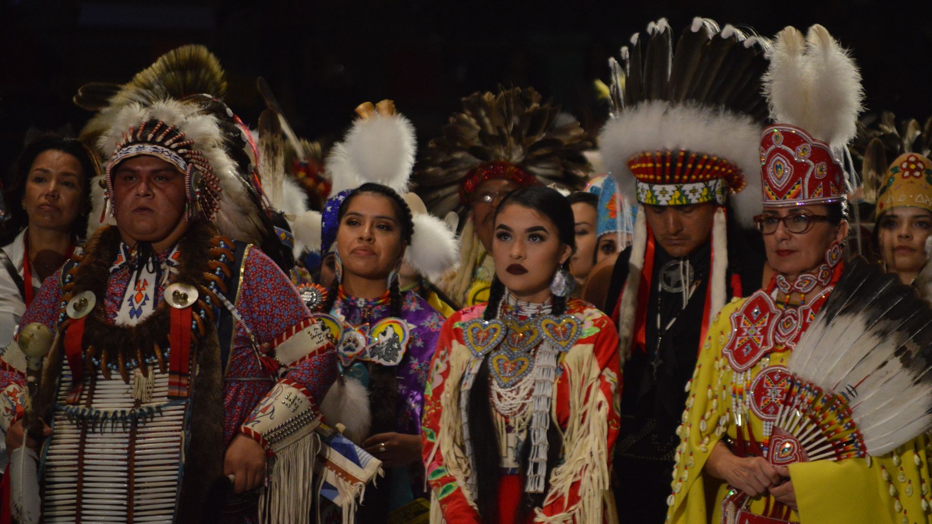 Group of people in traditional Native American regalia with colorful beadwork, feathered headdresses, and fringed garments at the Gathering of Nations in April 2017