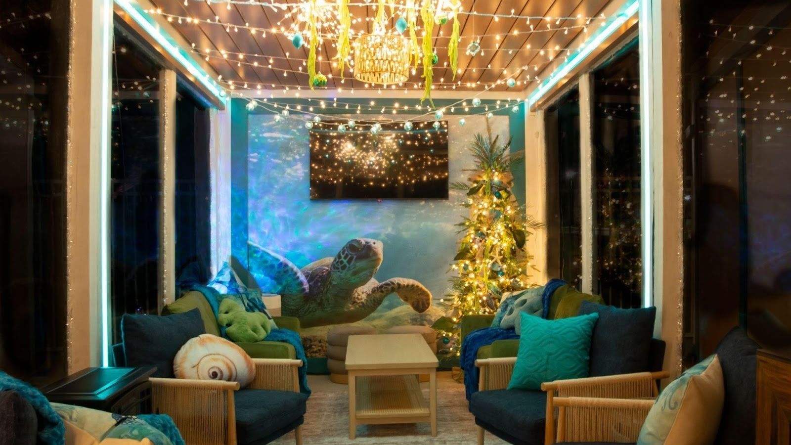 Enclosed cabana at Margaritaville decorated with sea turtle mural, string lights on ceiling, tropical-themed Christmas tree, blue and green cushions, and seashell pillows.