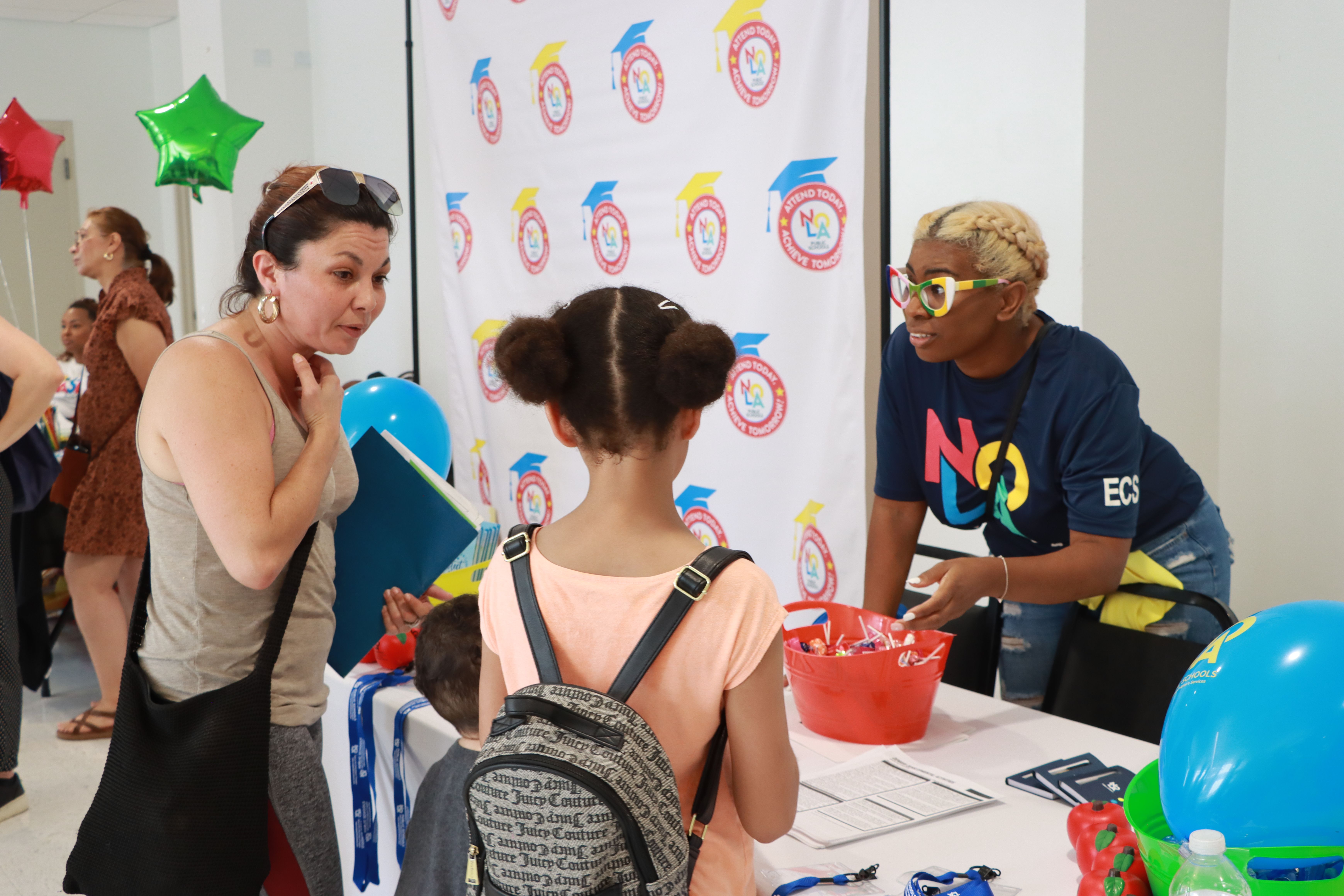 A young person approaches a table where two adults speak to her.