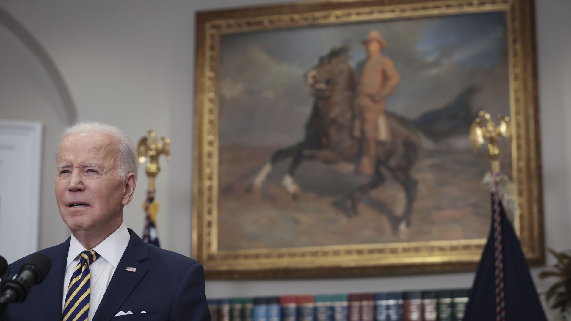 President Biden is seen speaking in front of a portrait of Teddy Roosevelt.