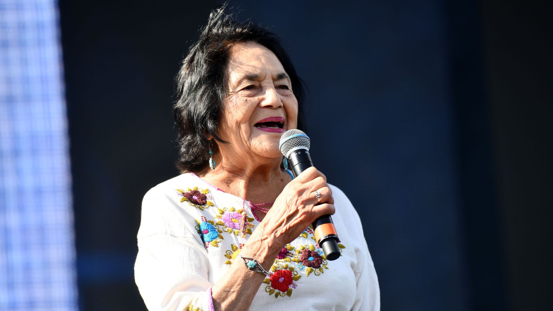 Mexican American civil rights icon Dolores Huerta, microphone in hand, delivers a speech.