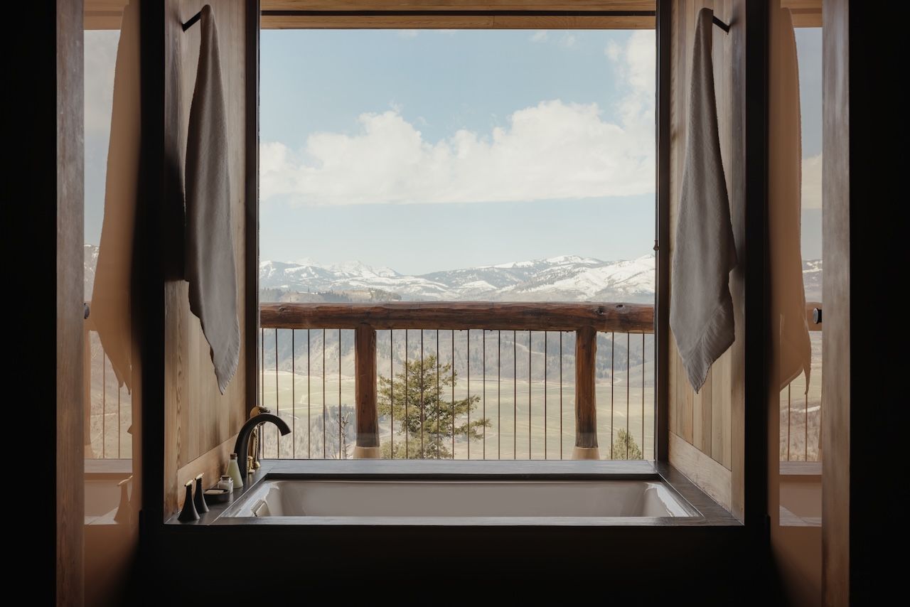 A photo of a bath tub facing out to a snow-capped mountain valley.