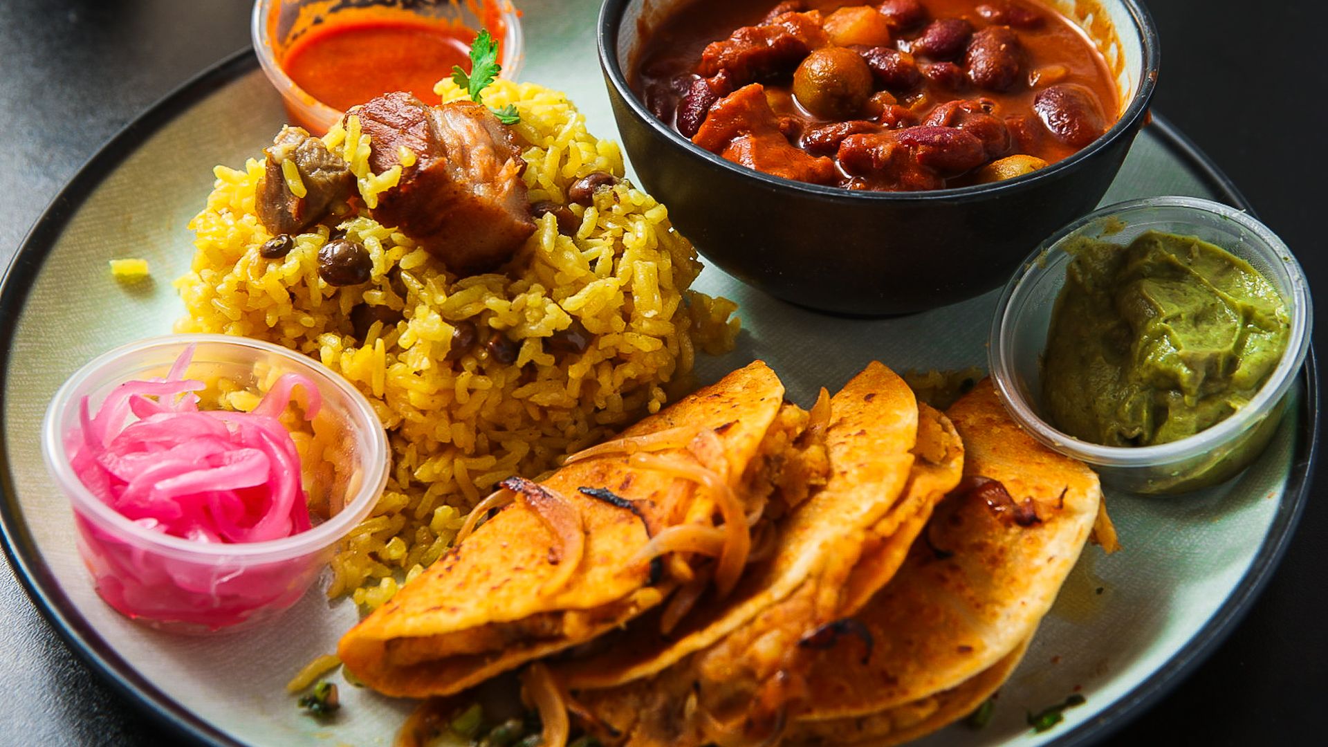 A plate with tacos, rice, beans and condiments. 