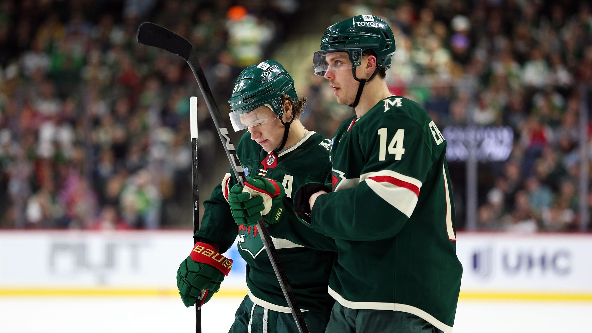 Two hockey players in green jerseys confer on the ice during a game