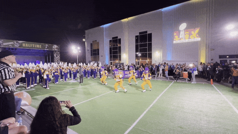 Drum majors dance in front of a marching band. 