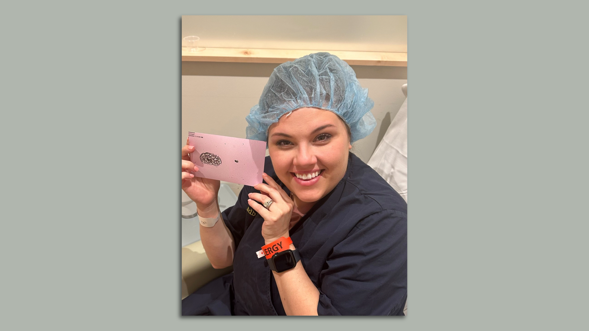 A woman wearing a hair net and scrubs holds up an image of her fertilized egg. 