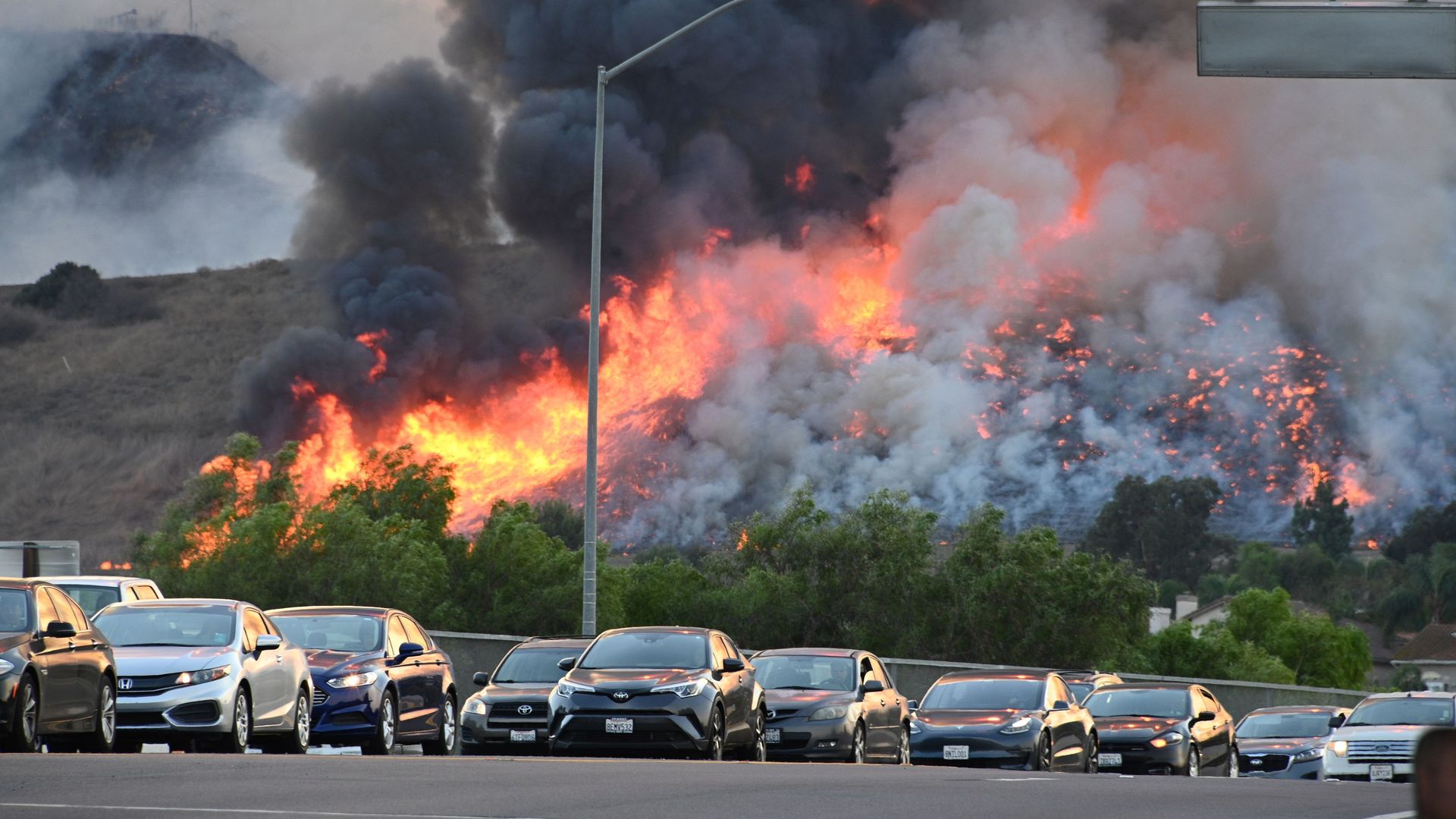 Flames are seen in the background as vehicles drive on a highway overpass at the Blue Ridge Fire in Chino, California, October 27